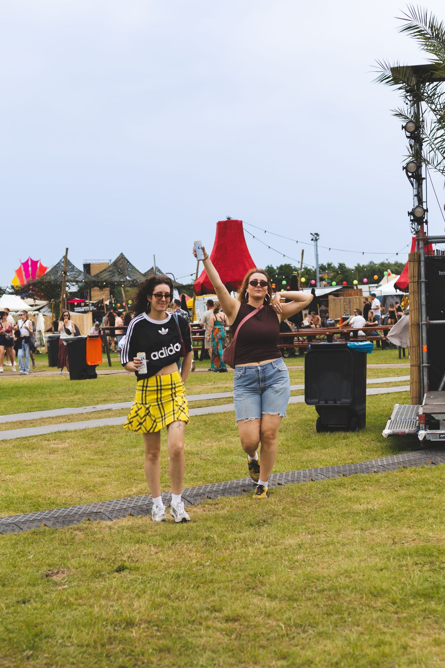 Two festival attendees dancing on grass field with tents and palm trees in background.