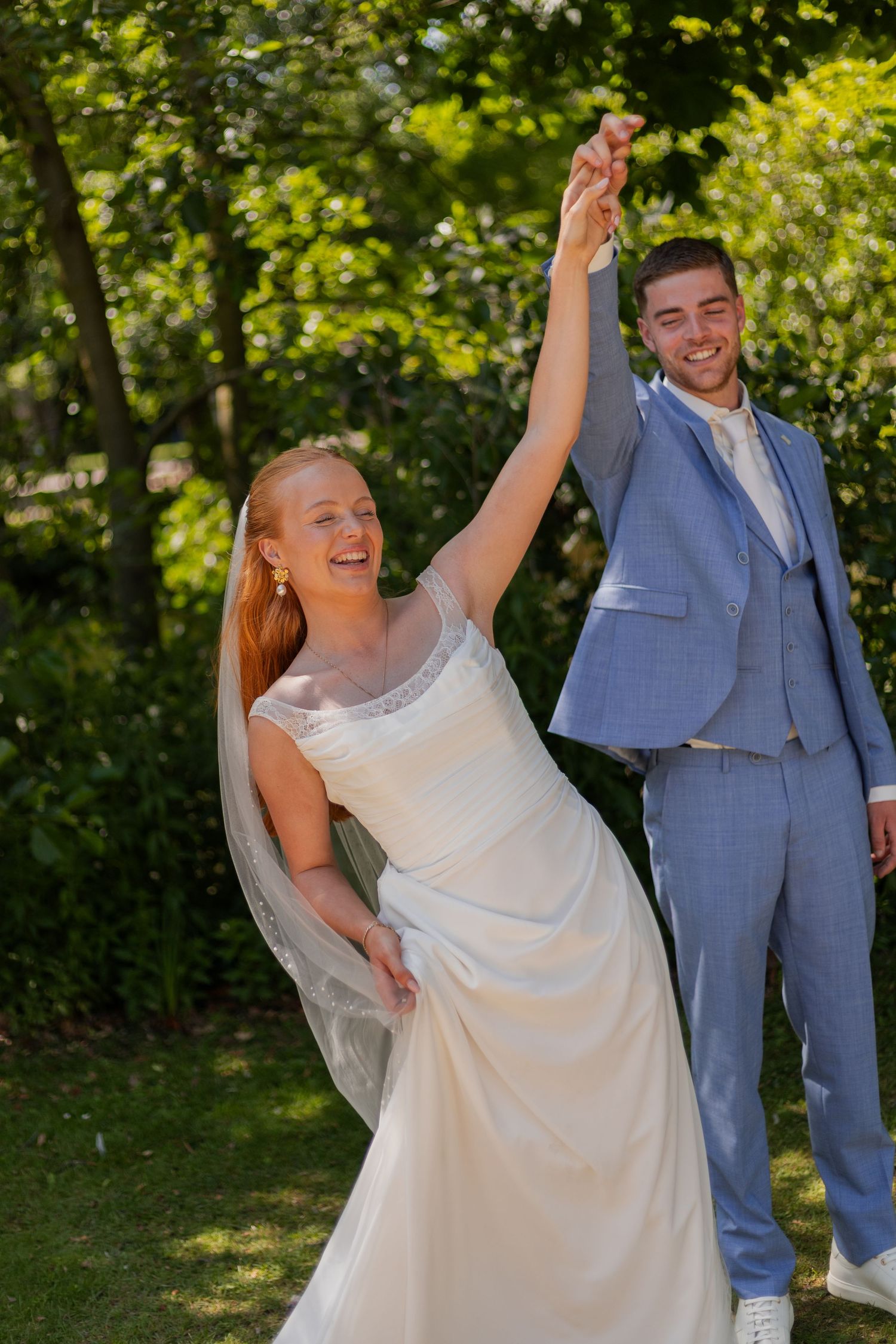 A wedding couple dances joyfully together in a sunny garden setting.