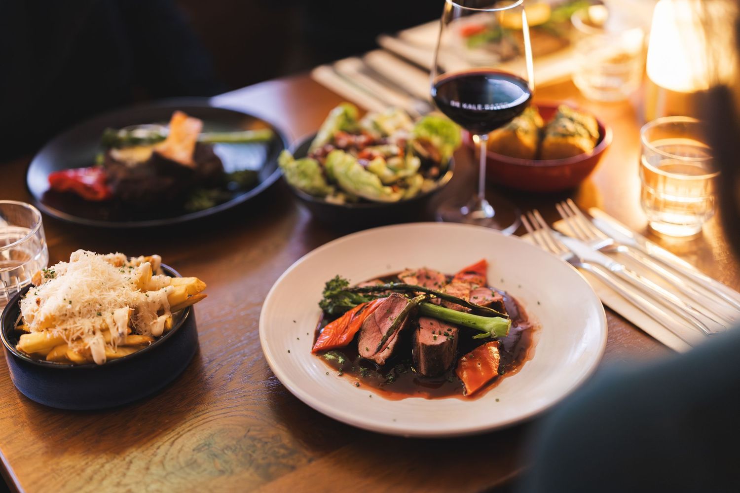 Elegant restaurant table setting with multiple plates of gourmet food and soft candlelight ambiance.