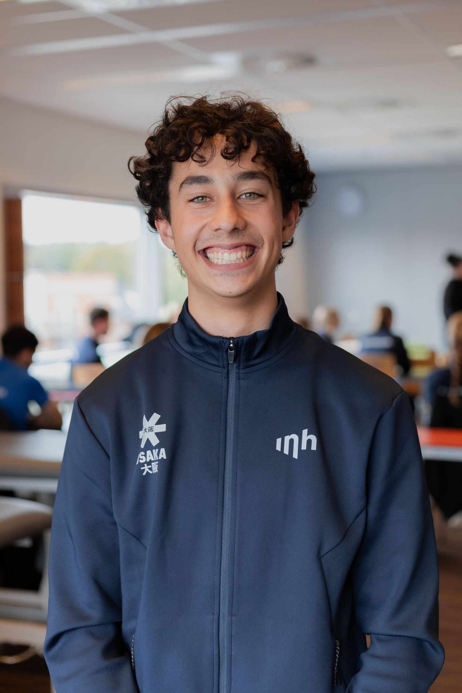 A person wearing a navy blue zip-up jacket smiles warmly in a series of similar indoor portraits.