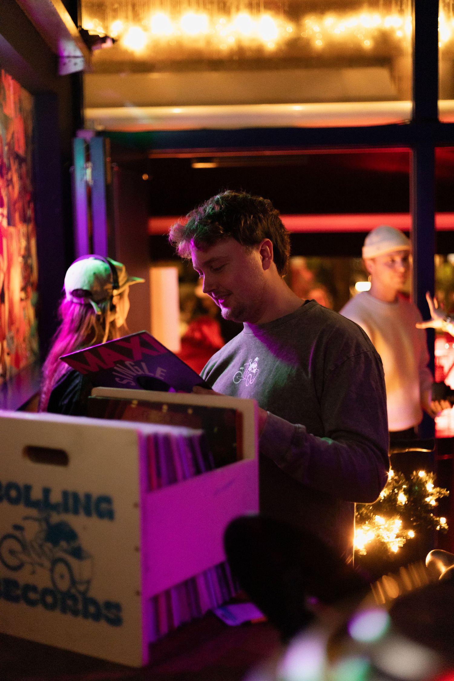 Record store customers flip through albums under warm string lights and neon signage.