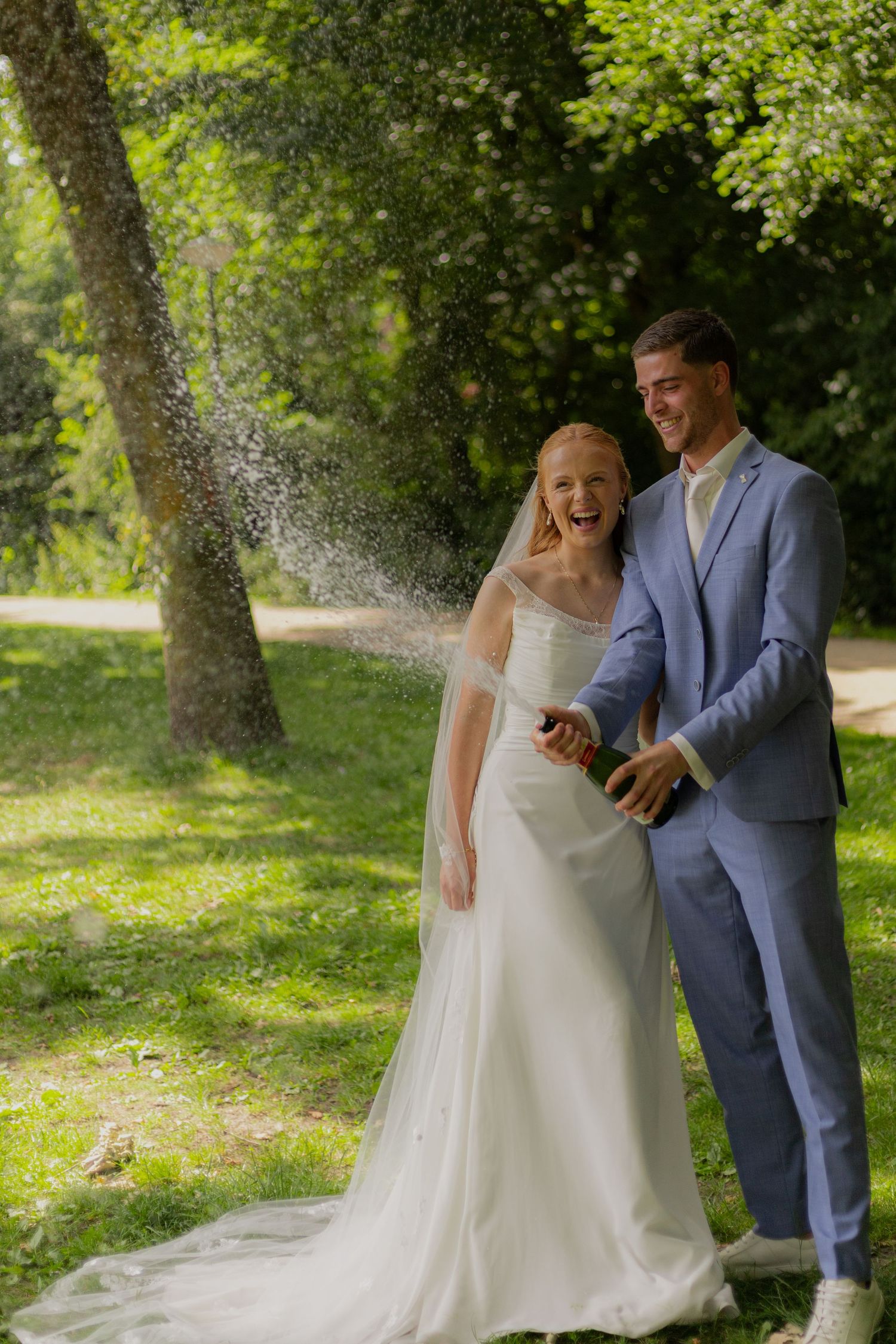 Wedding couple sprays champagne outdoors in a playful celebration moment.