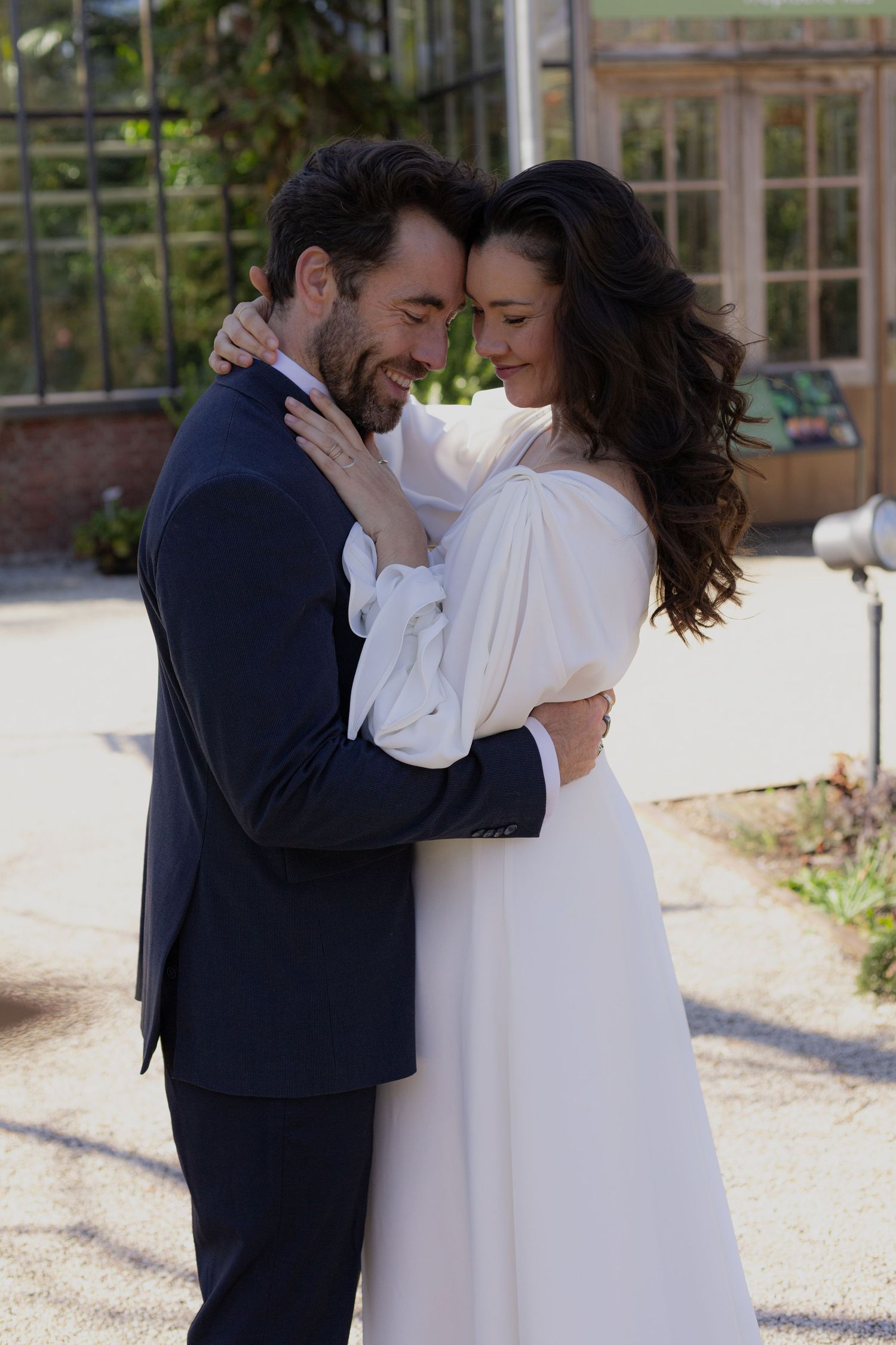 Romantic wedding photos of couple in white dress and dark suit on sunny pathway.