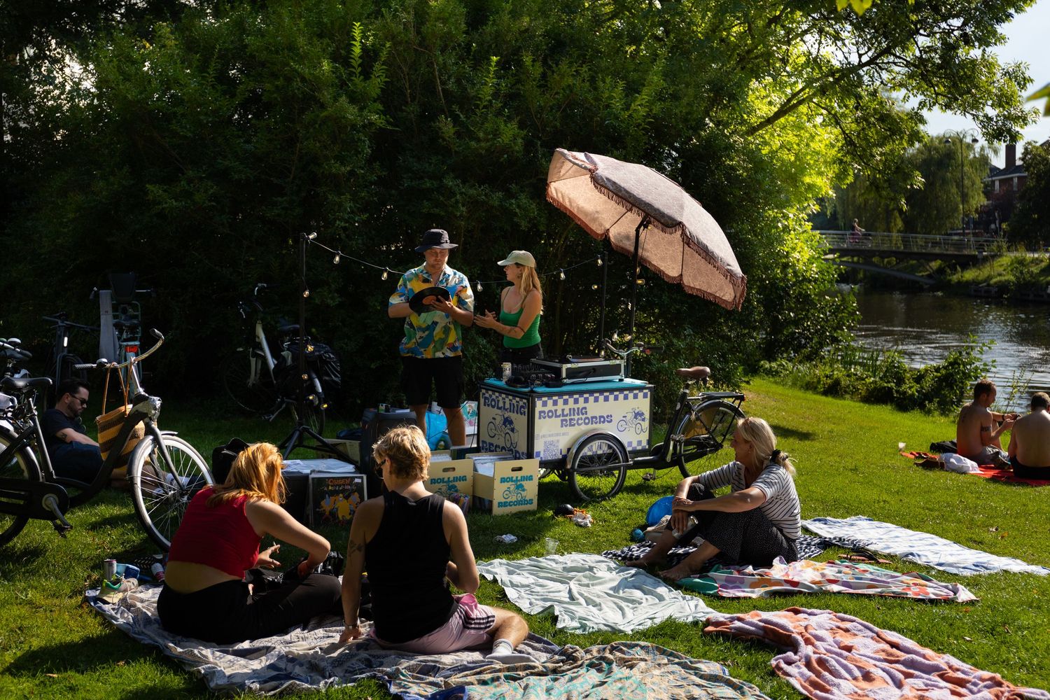 Group of people relaxing on blankets at an outdoor music event near water.