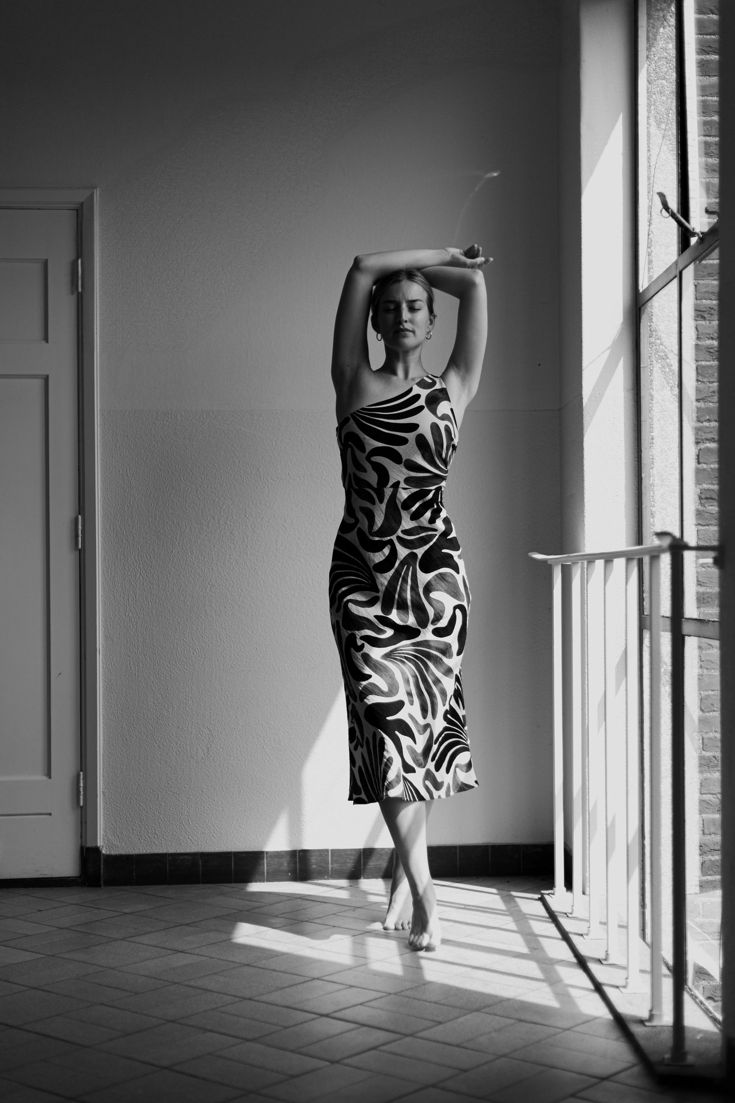 Dramatic black and white photos of a person in patterned dress posing near sunlit windows.