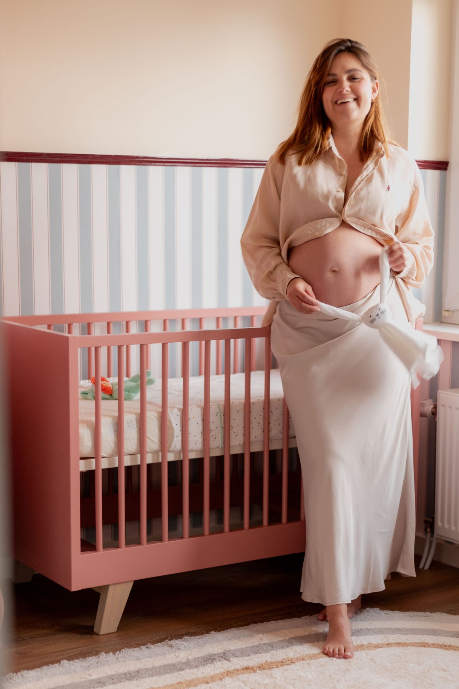 A series of four intimate maternity photos showing a person in a white dress sitting near a pink baby crib.