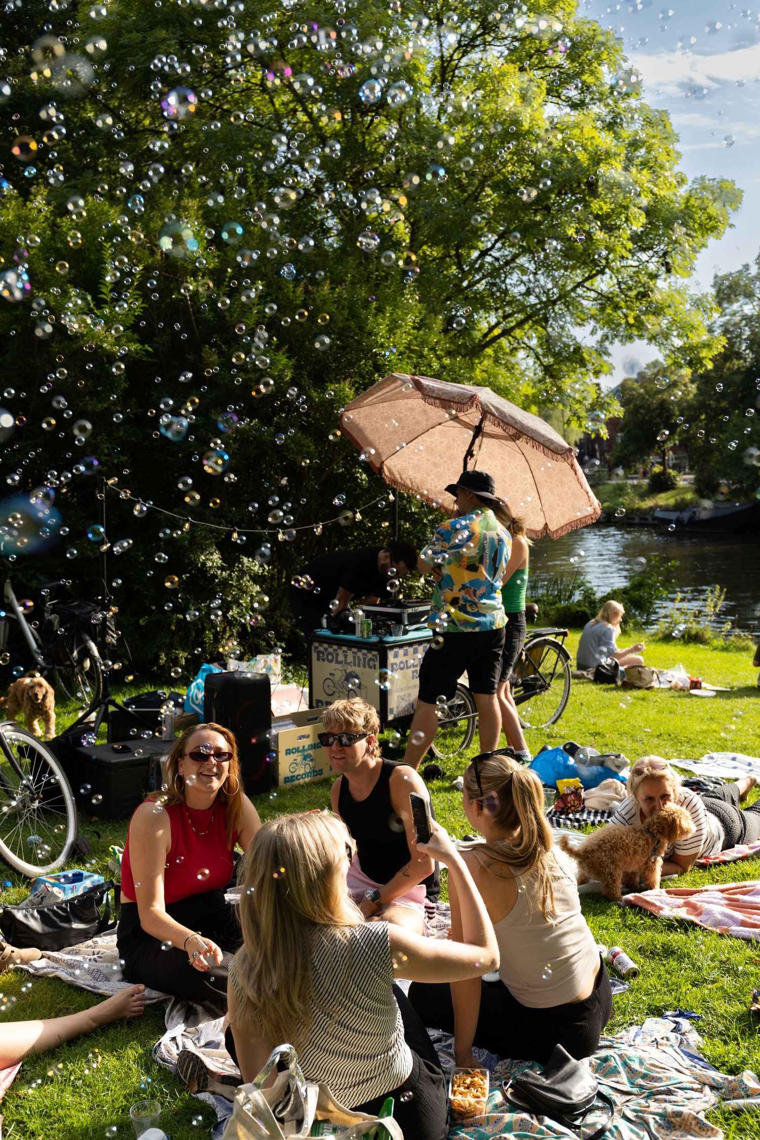 Friends enjoying drinks and conversation under trees at a summer outdoor gathering.