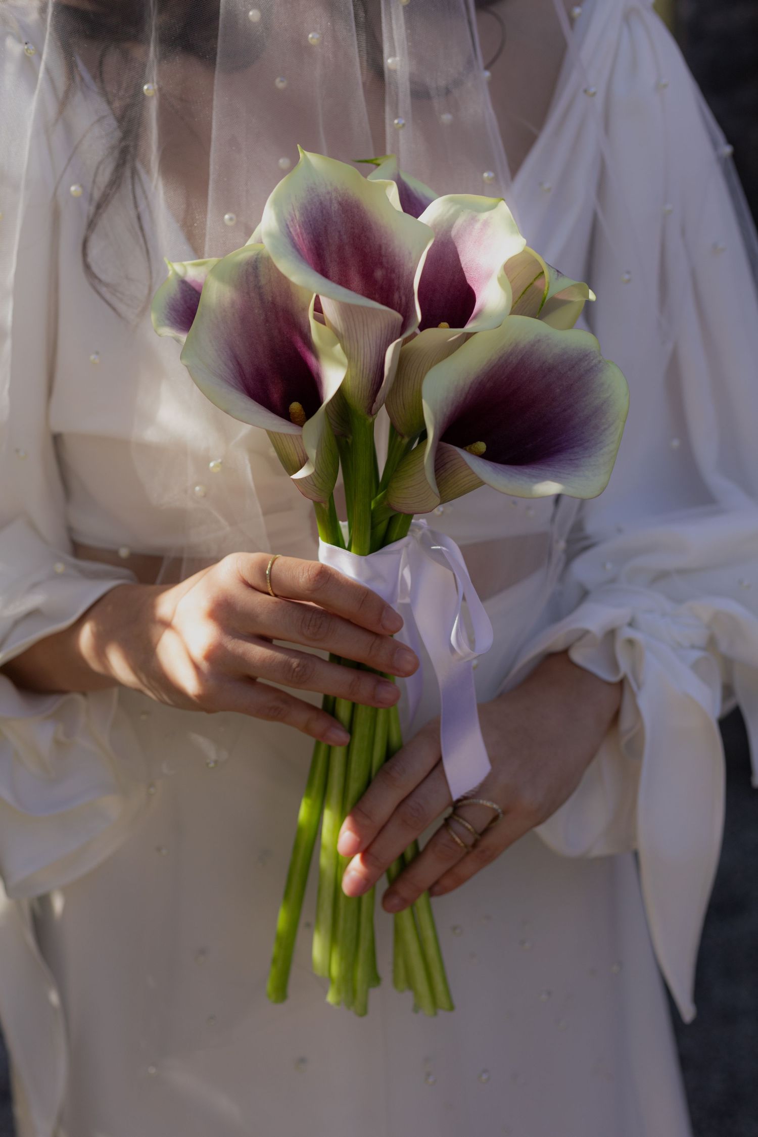 Delicate purple and white calla lily bouquet held against a white gown.