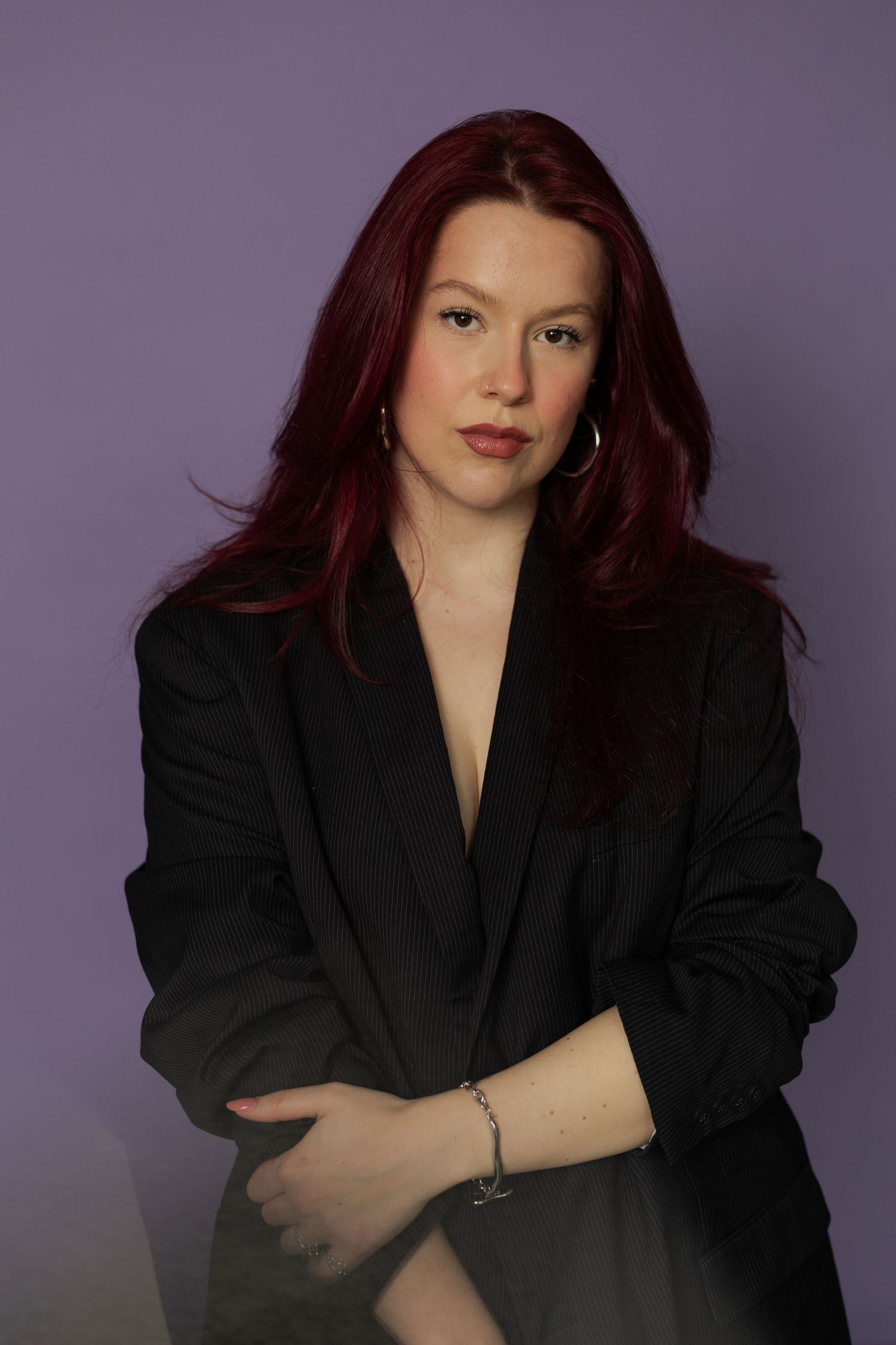 Professional studio portrait series against purple background featuring model in black blazer with auburn hair.