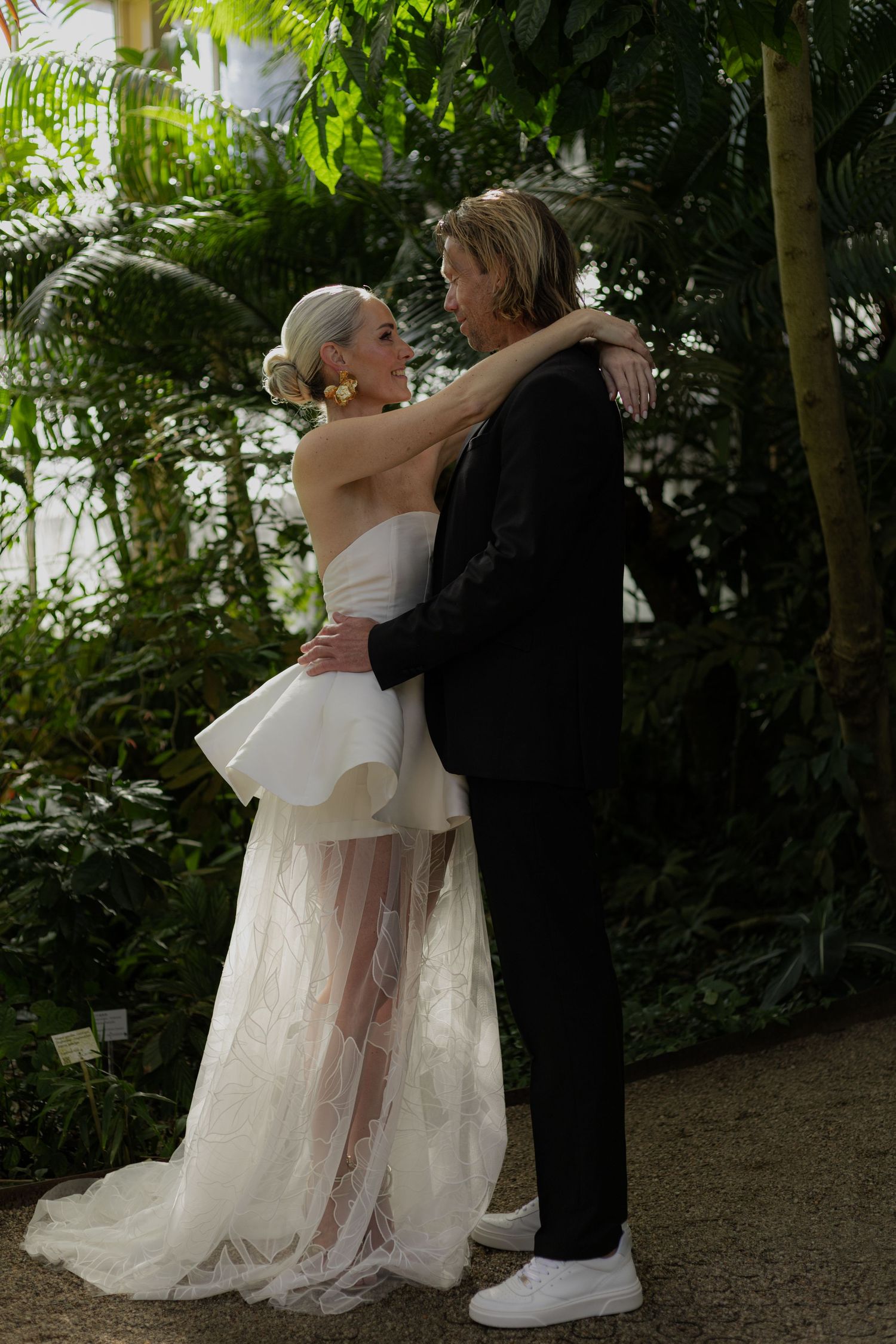 Wedding couple embraces on a garden path surrounded by lush greenery.