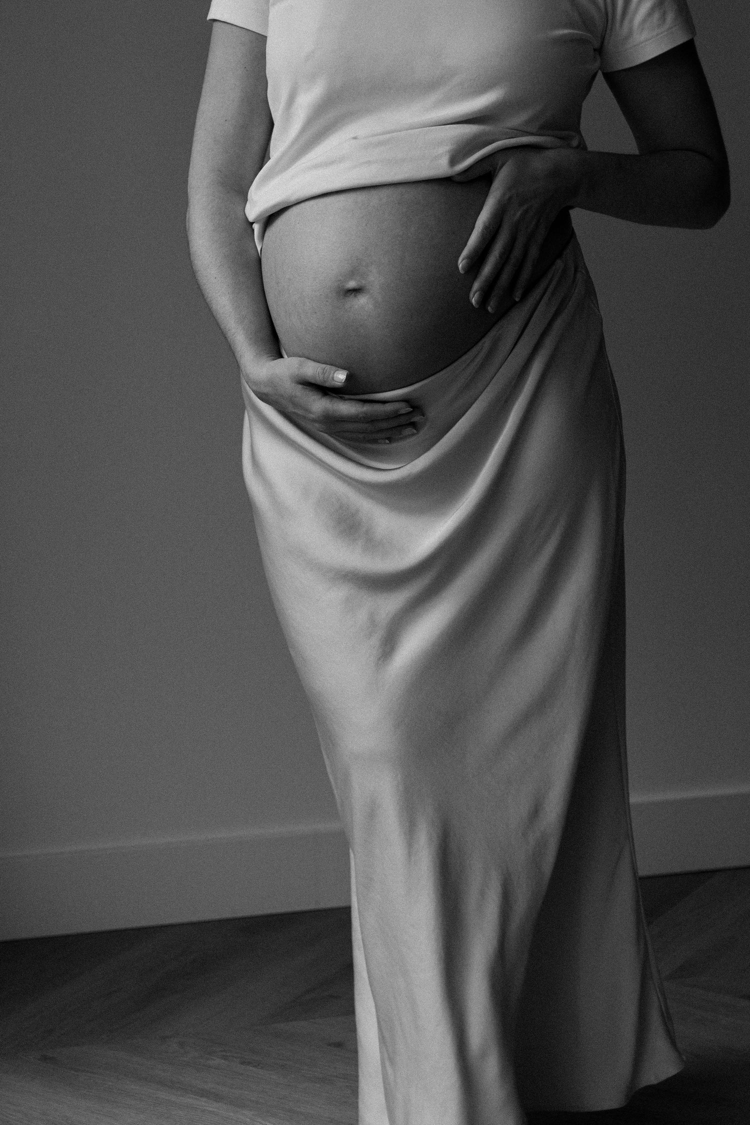 Black and white photo series showing progression of pregnancy with woman wearing flowing dress in side profile poses.