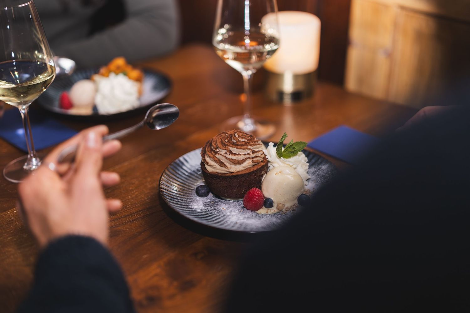 Four glasses of wine and a chocolate dessert are arranged on a rustic wooden table at a restaurant.
