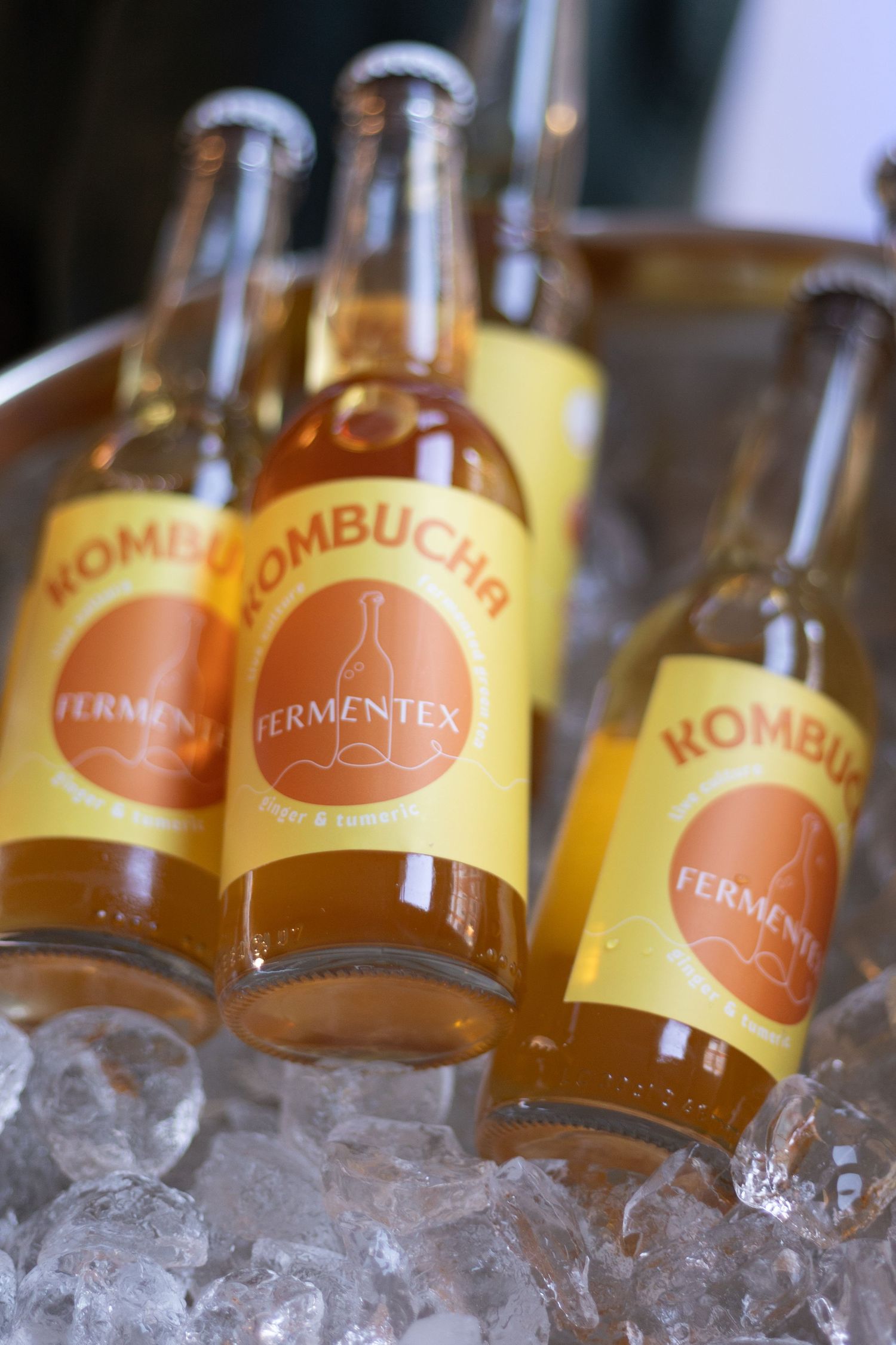 Kombucha bottles lined up on ice showing orange and yellow branded labels.