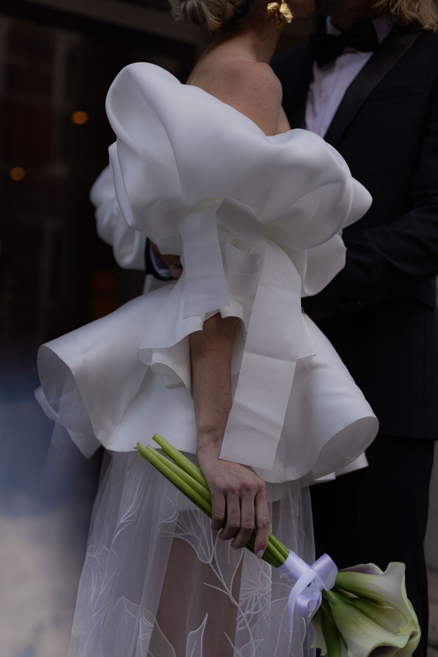Close-up of a bride's dramatic white ruffled wedding dress shoulder detail and calla lily bouquet.