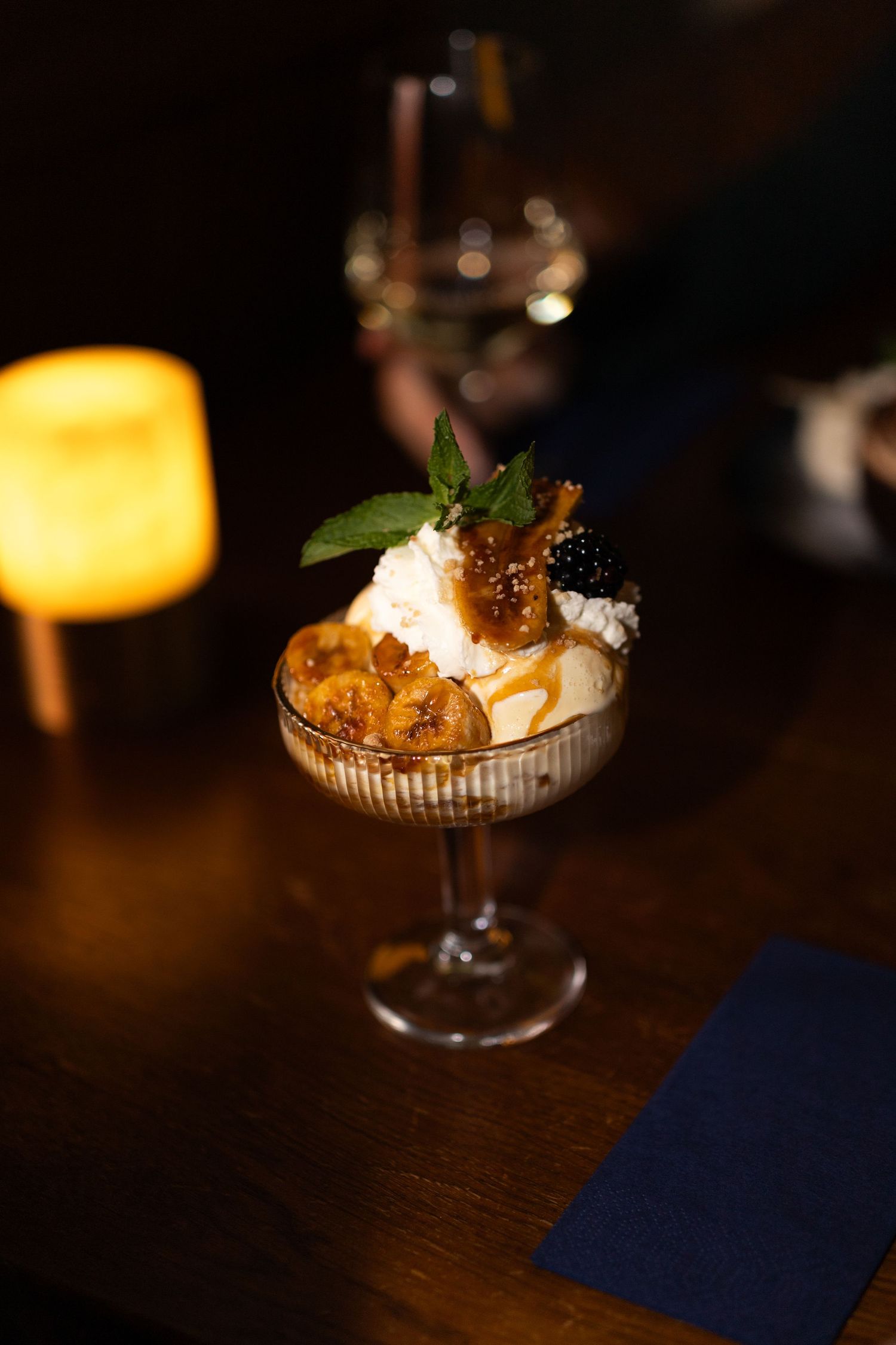 Elegant dessert presentations in glass bowls with whipped cream and garnishes in a dimly lit restaurant setting.