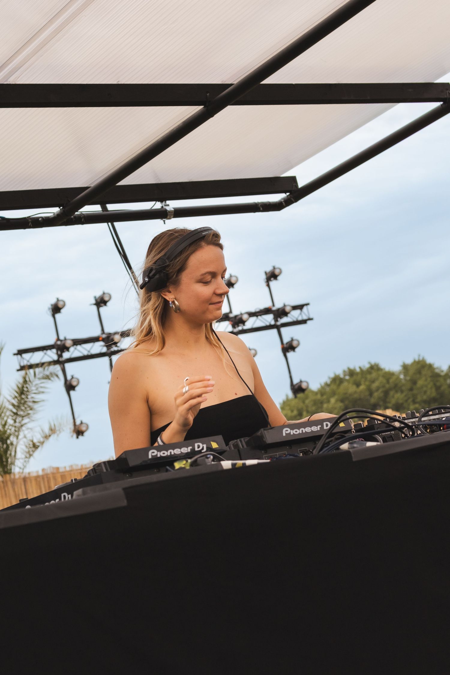 DJ performing on outdoor stage with Pioneer equipment during daytime festival.