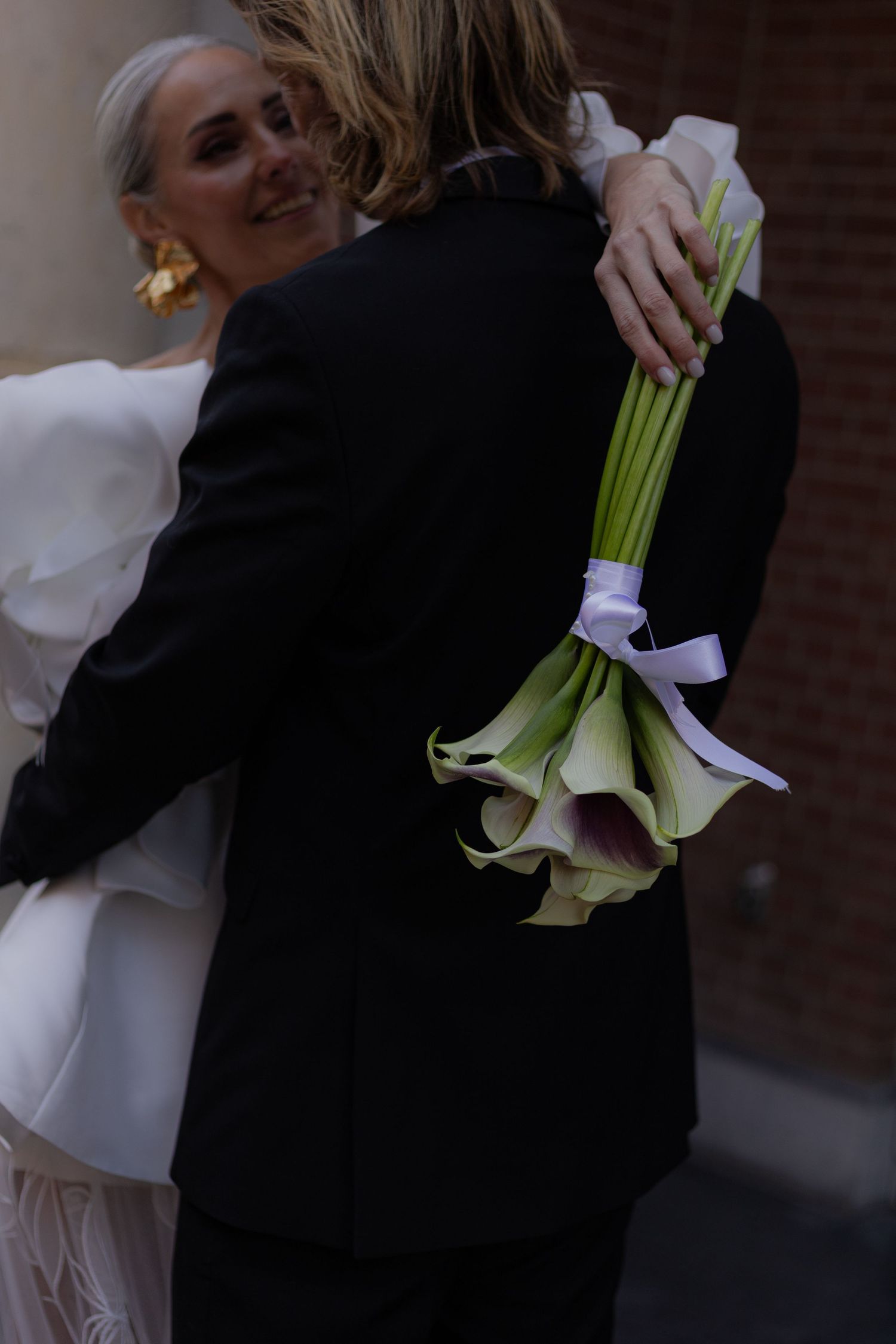A tender embrace captured at a wedding, with elegant white dress details and calla lilies.