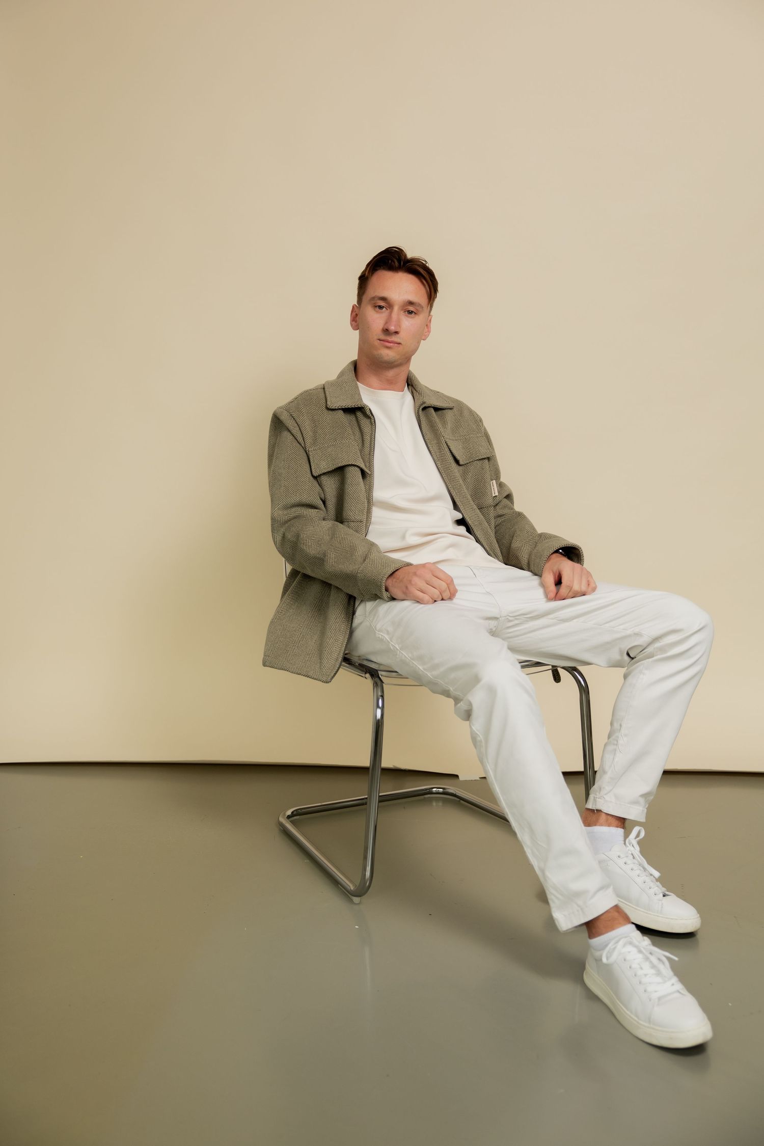 A person in a casual outfit of white t-shirt, khaki jacket and white pants sits in various poses on a modern chair.