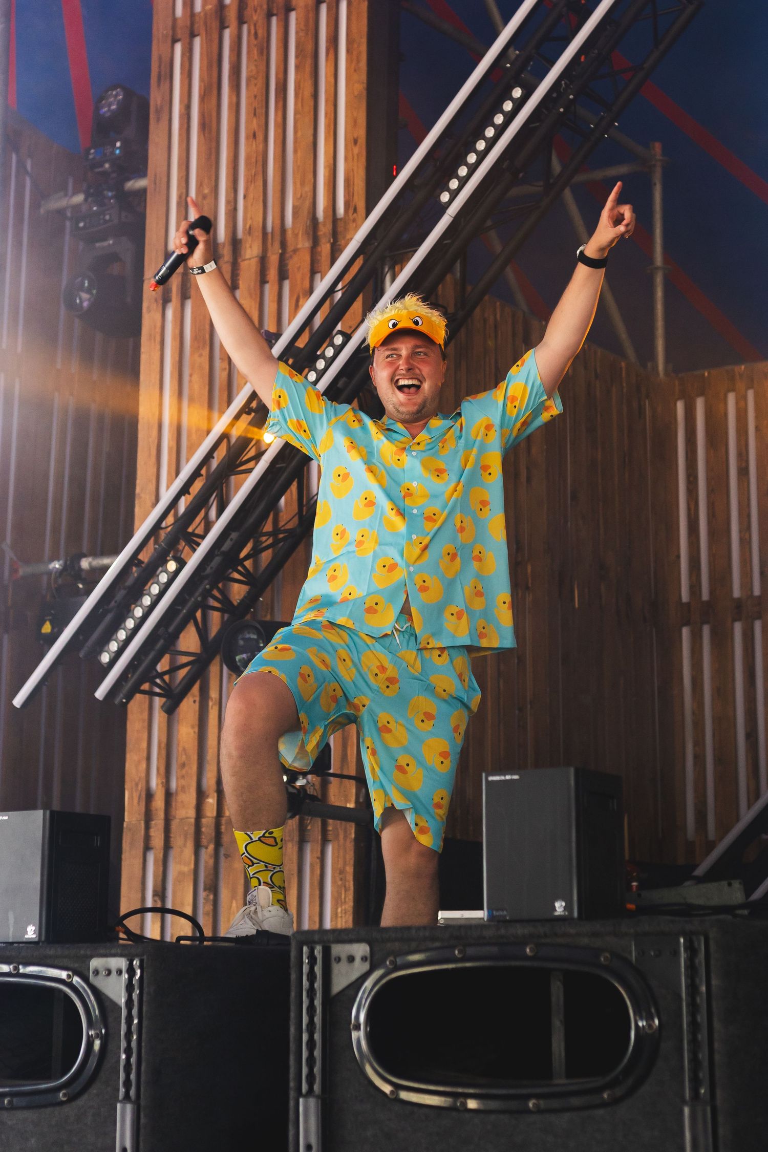 Energetic performer in bright turquoise outfit dancing on stage with dramatic lighting.
