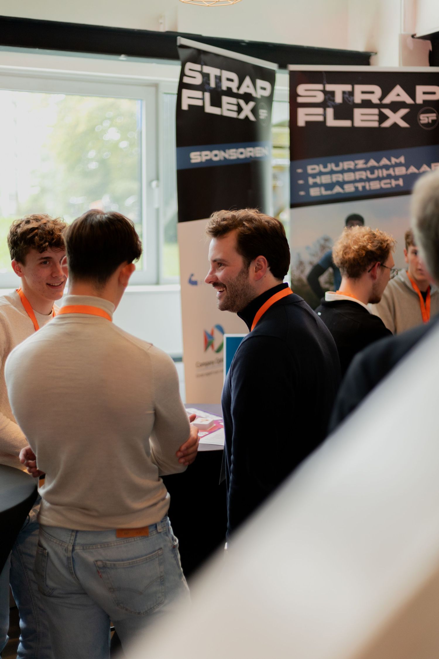 People gather around a Strapflex sponsor booth at a business networking event having conversations.