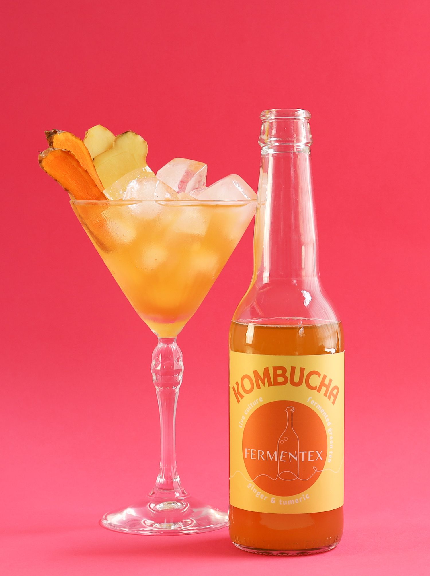 Kombucha cocktails with orange garnish displayed against a vibrant pink background.
