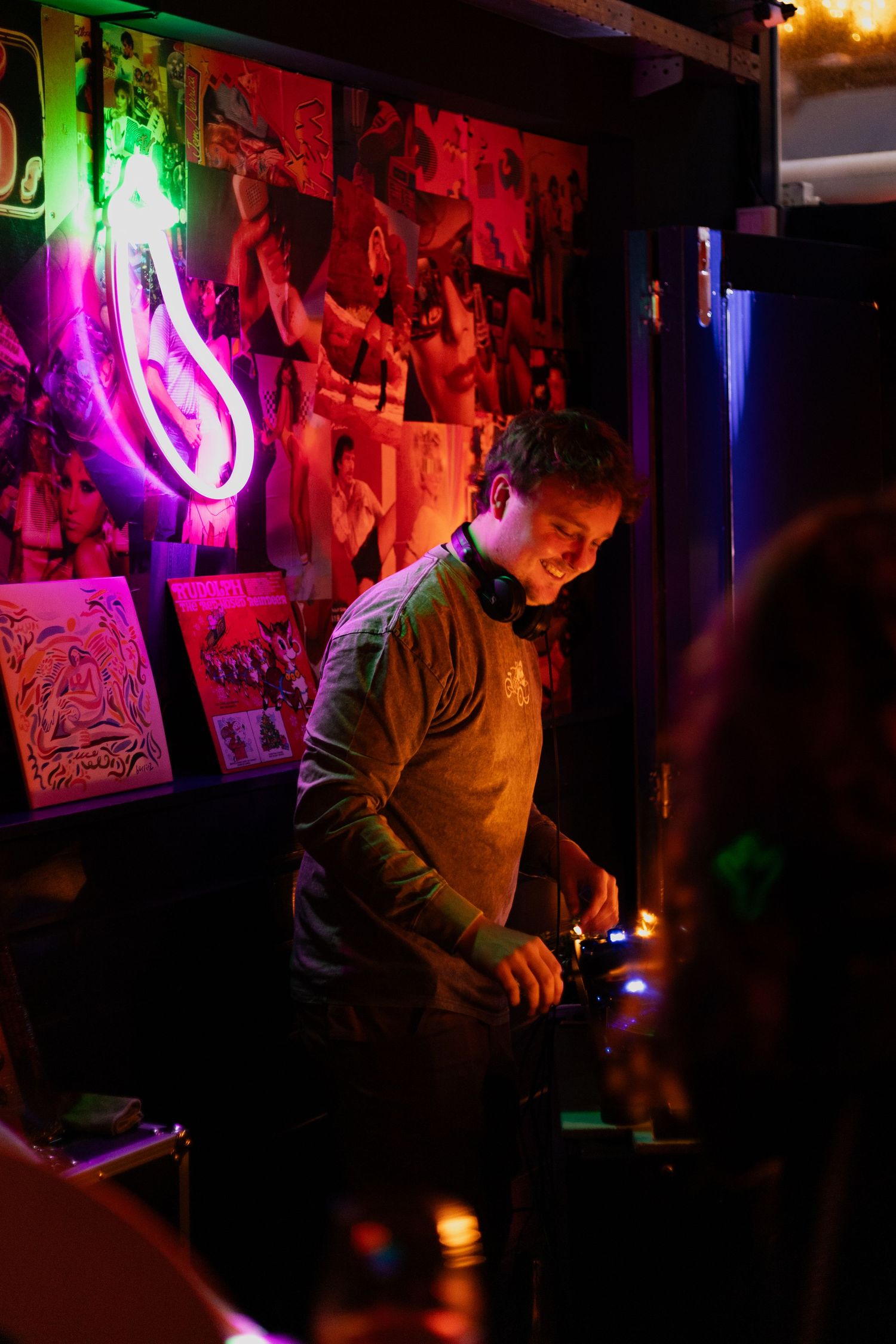 DJ performs in a dark nightclub setting with vibrant red and green neon lights illuminating the space.