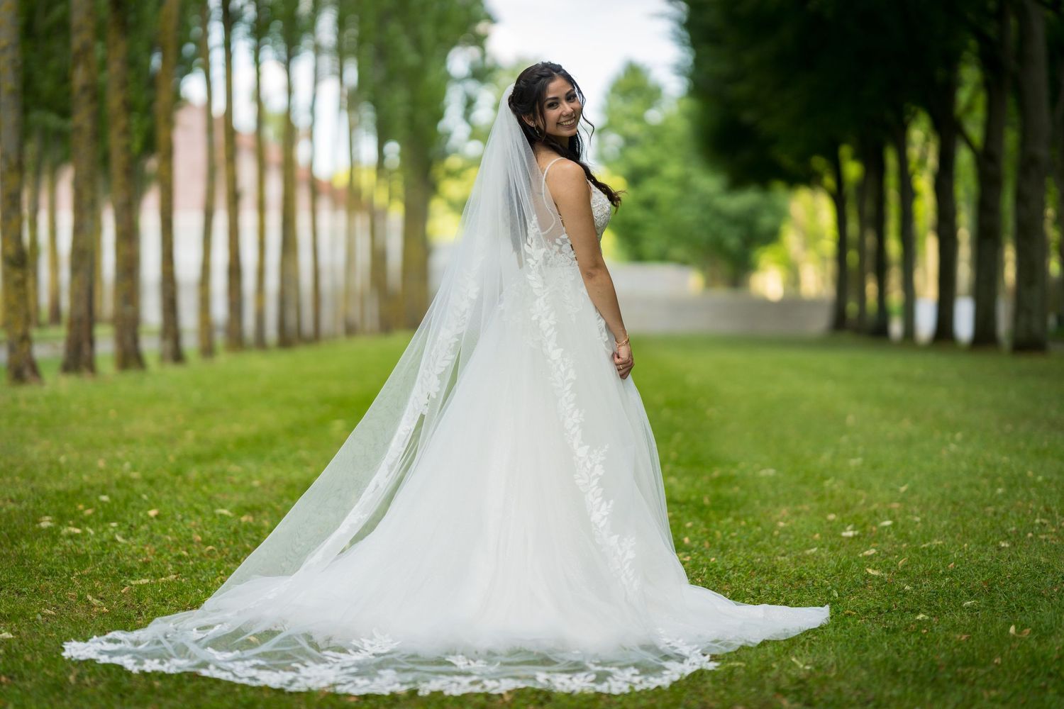 Braut im Hochzeitskleid mit langem Schleier auf einer Baumallee im Treptower Park Berlin