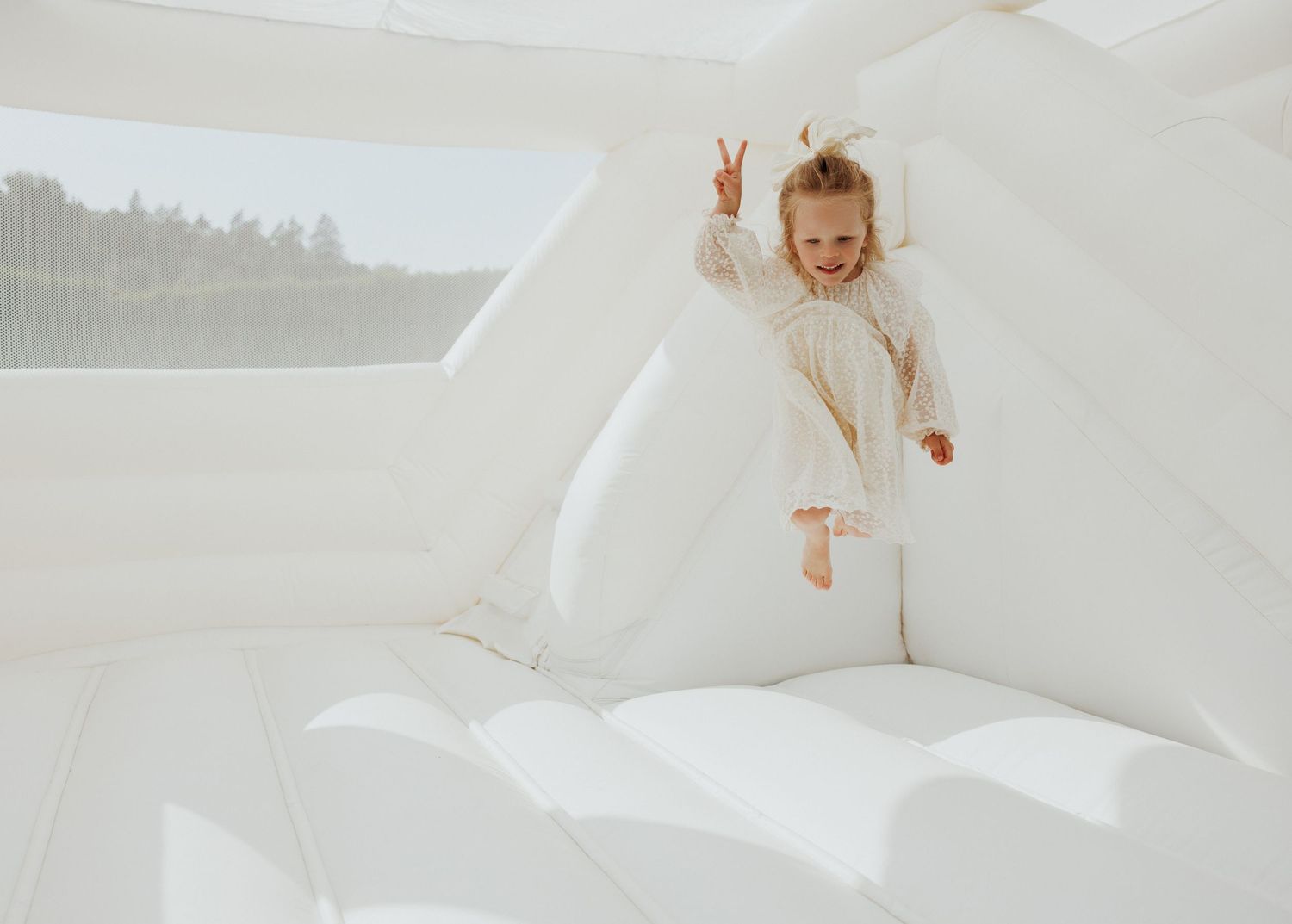 A dreamy ethereal photoshoot featuring a figure in flowing white fabric against a light background.