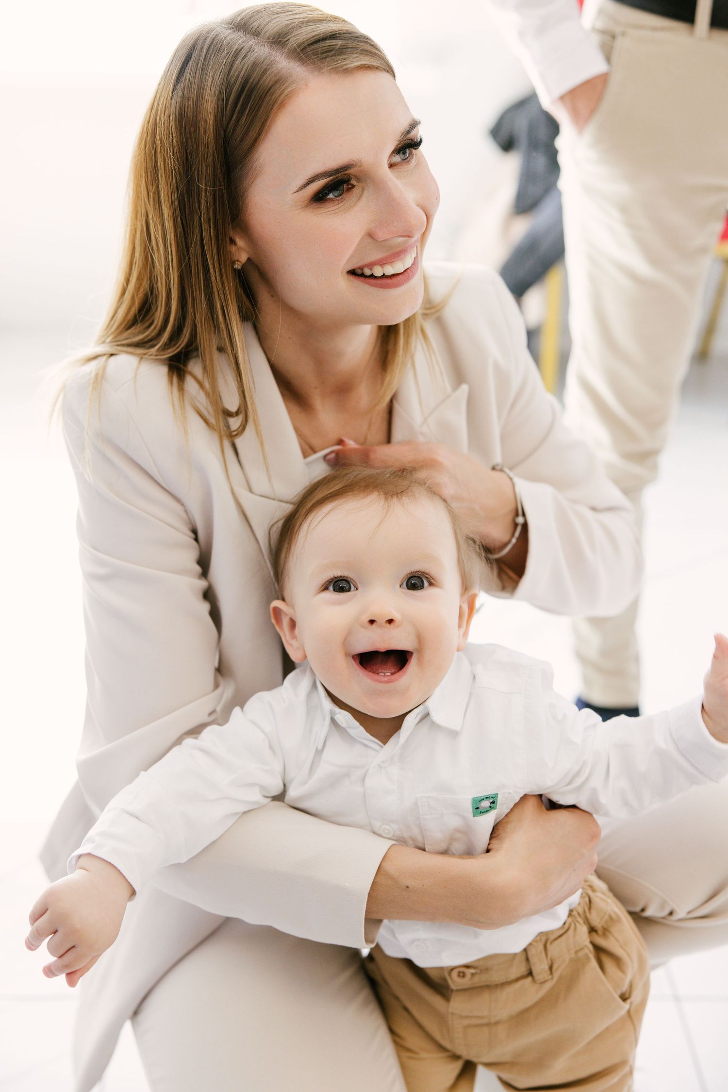 Sweet family portrait session in white outfits shows tender moments between parent and baby on light background.