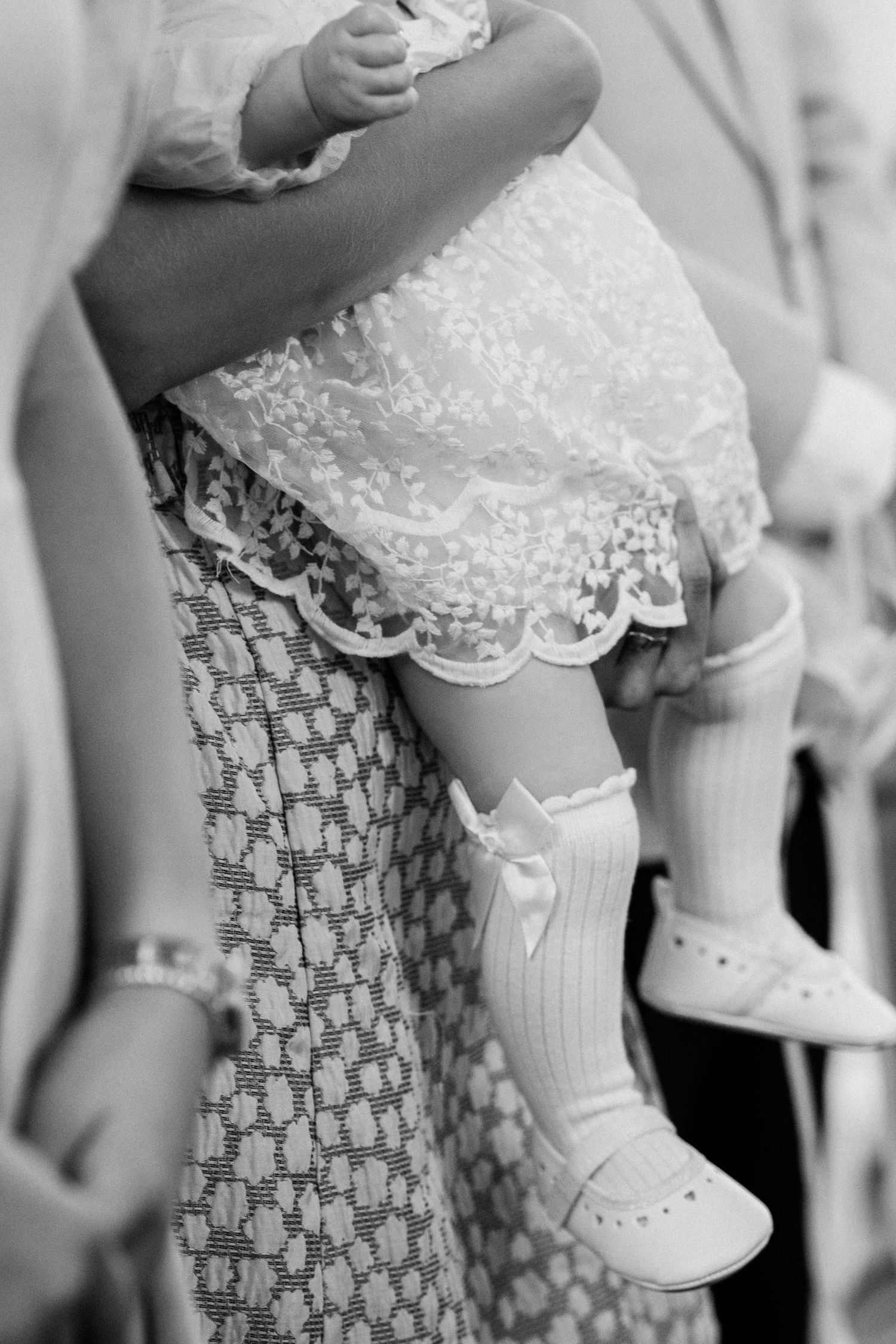 Close-up black and white photo of baby feet wearing white lace socks and traditional white leather shoes.