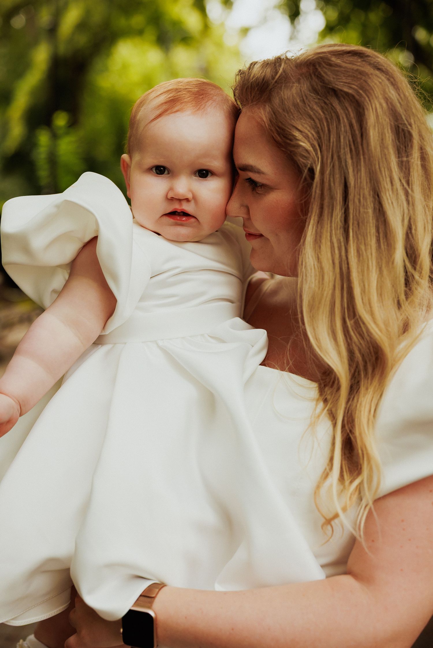 Tender moment captured in natural light with baby wearing elegant white dress.