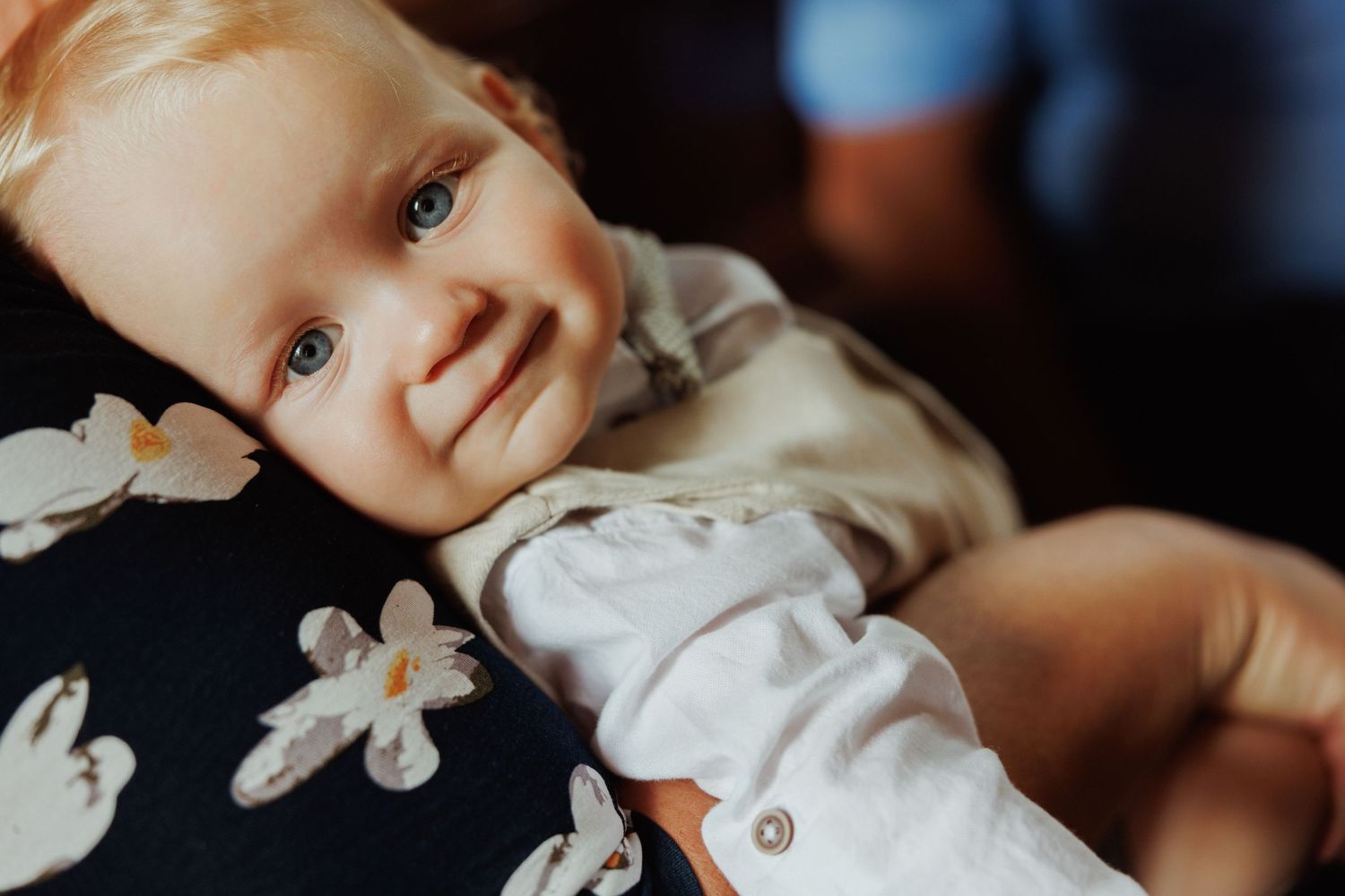 A baby in white clothing lies on a dark surface with a soft, dreamy expression.