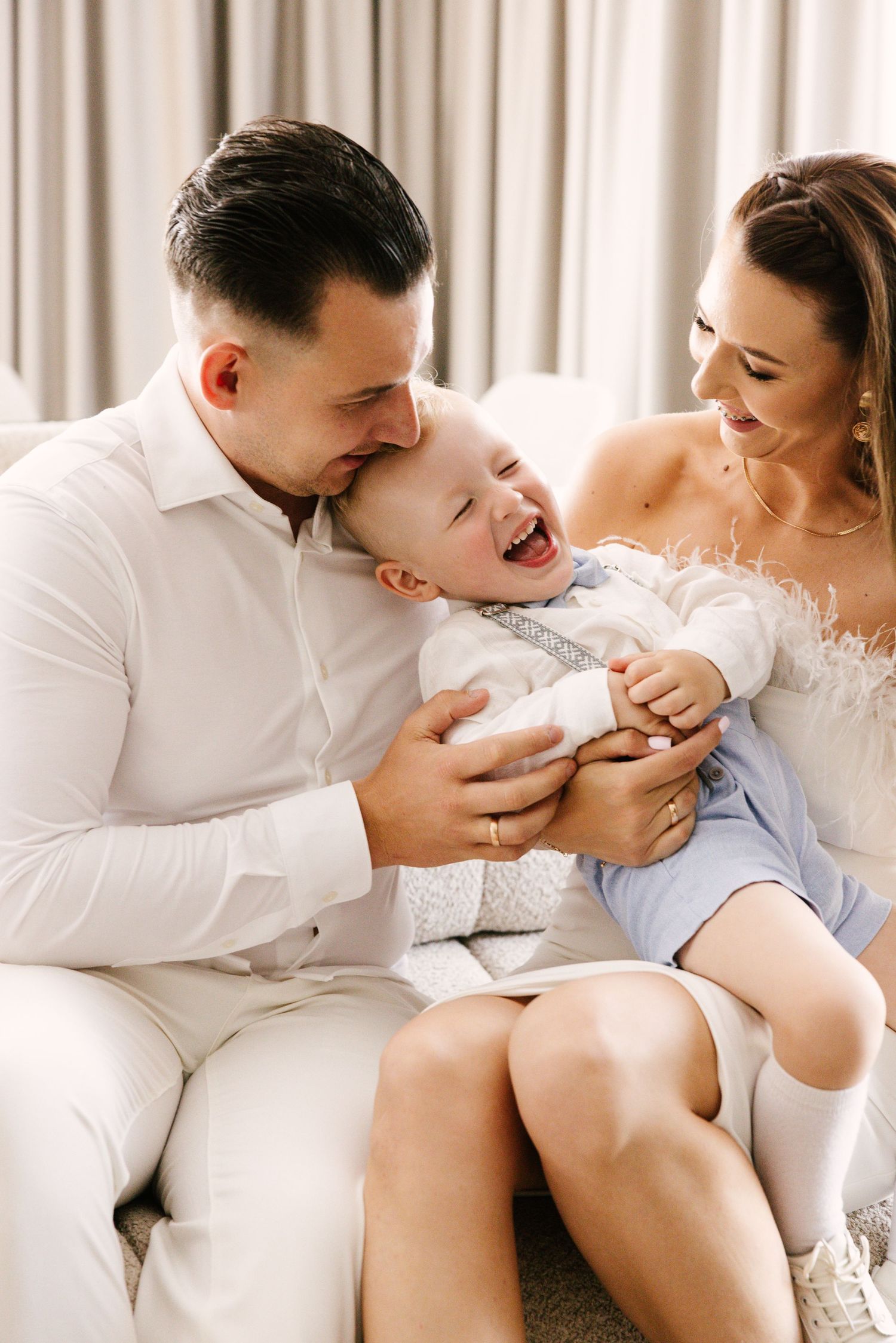 Tender family moment captured on white sofa in bright interior setting.