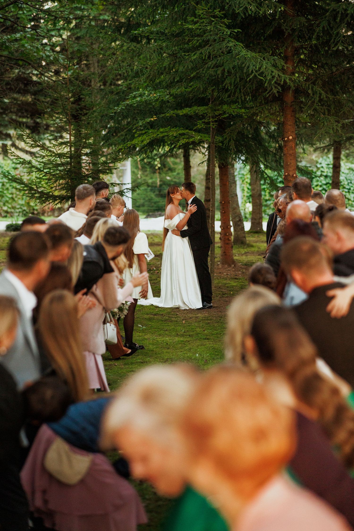Outdoor wedding ceremony in a wooded setting with guests gathered to witness the occasion.