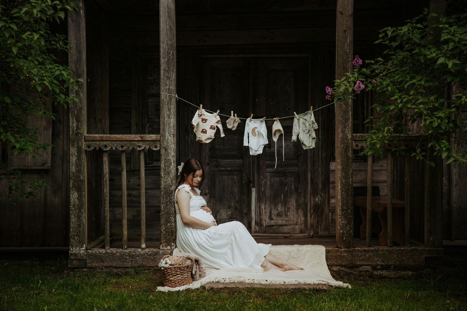 Maternity photo with baby clothes hanging on clothesline against rustic barn backdrop.