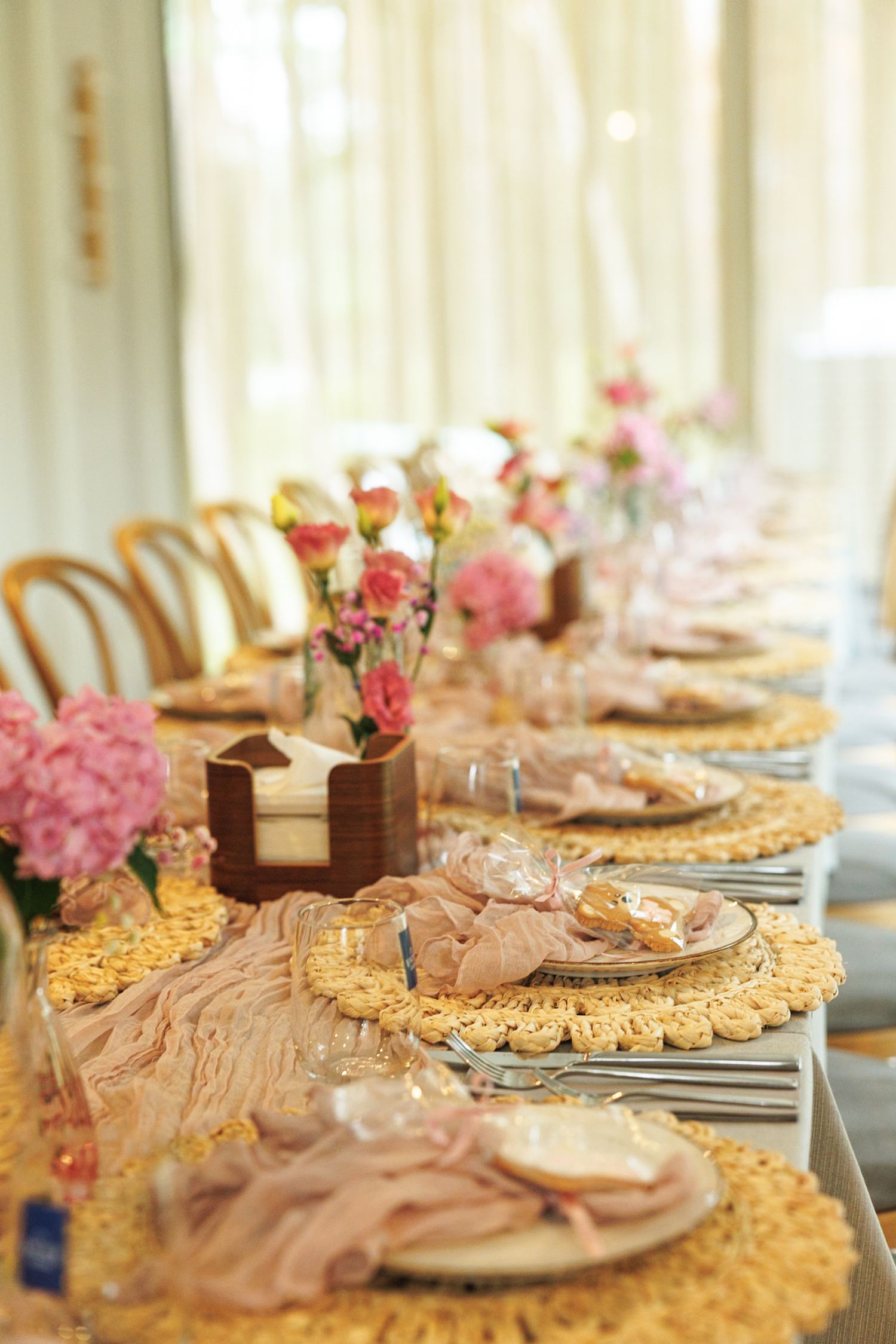 Formal table setting with gold charger plates, pink floral centerpieces, and taupe linens.