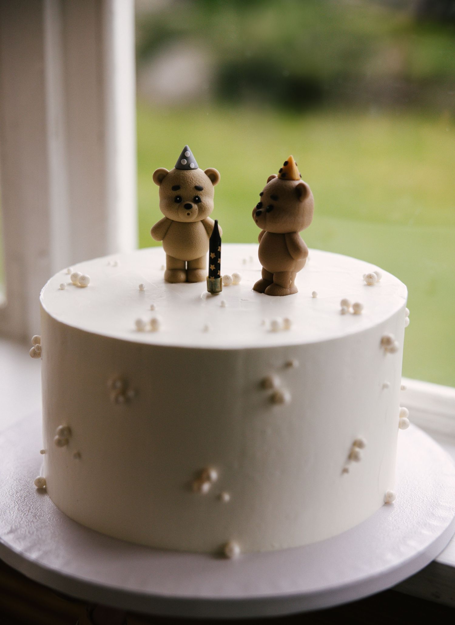 Minimalist white cake decorated with tiny teddy bear figurines on top.