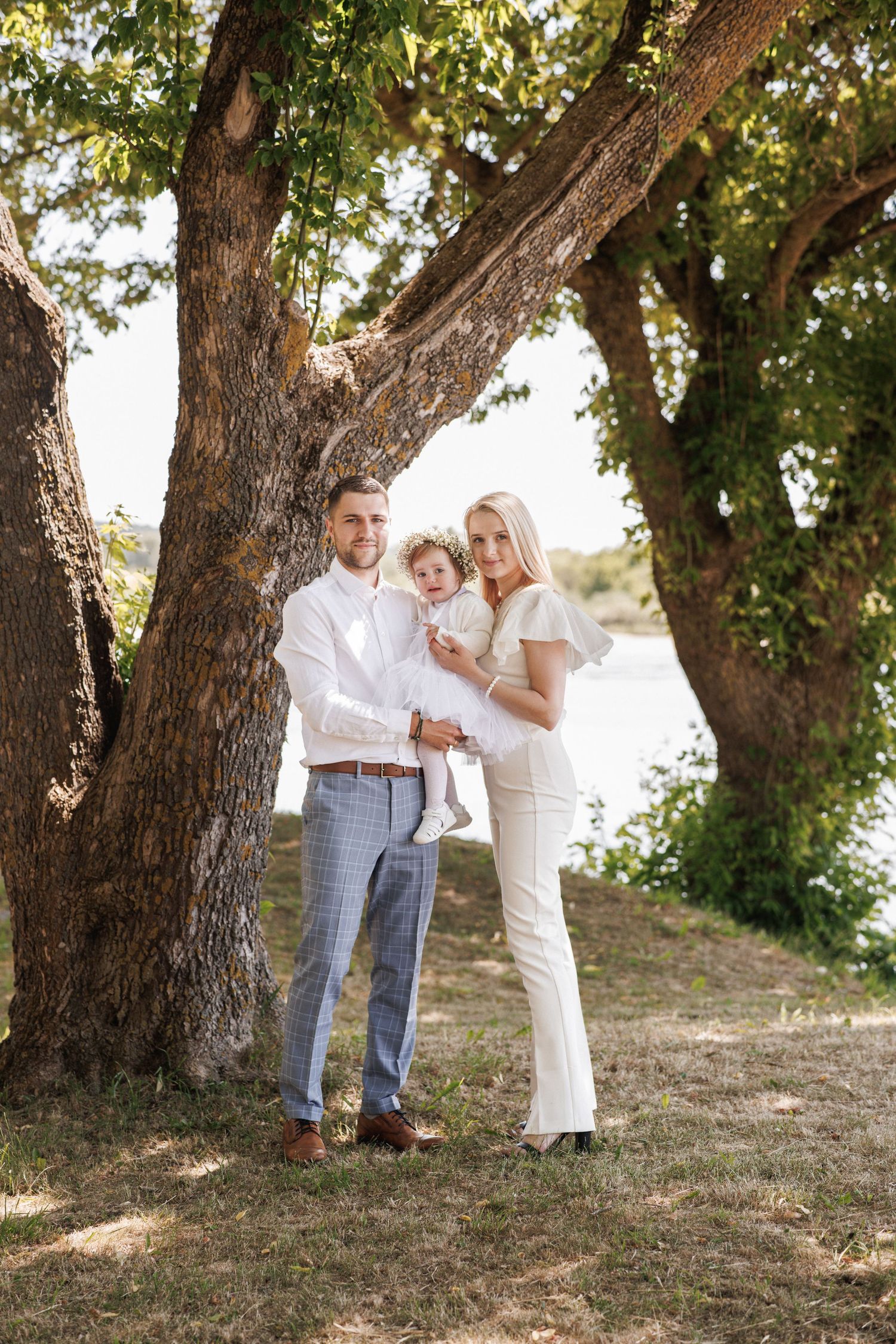 A family in white outfits poses together in a series of candid moments under large oak trees during a sunny day.