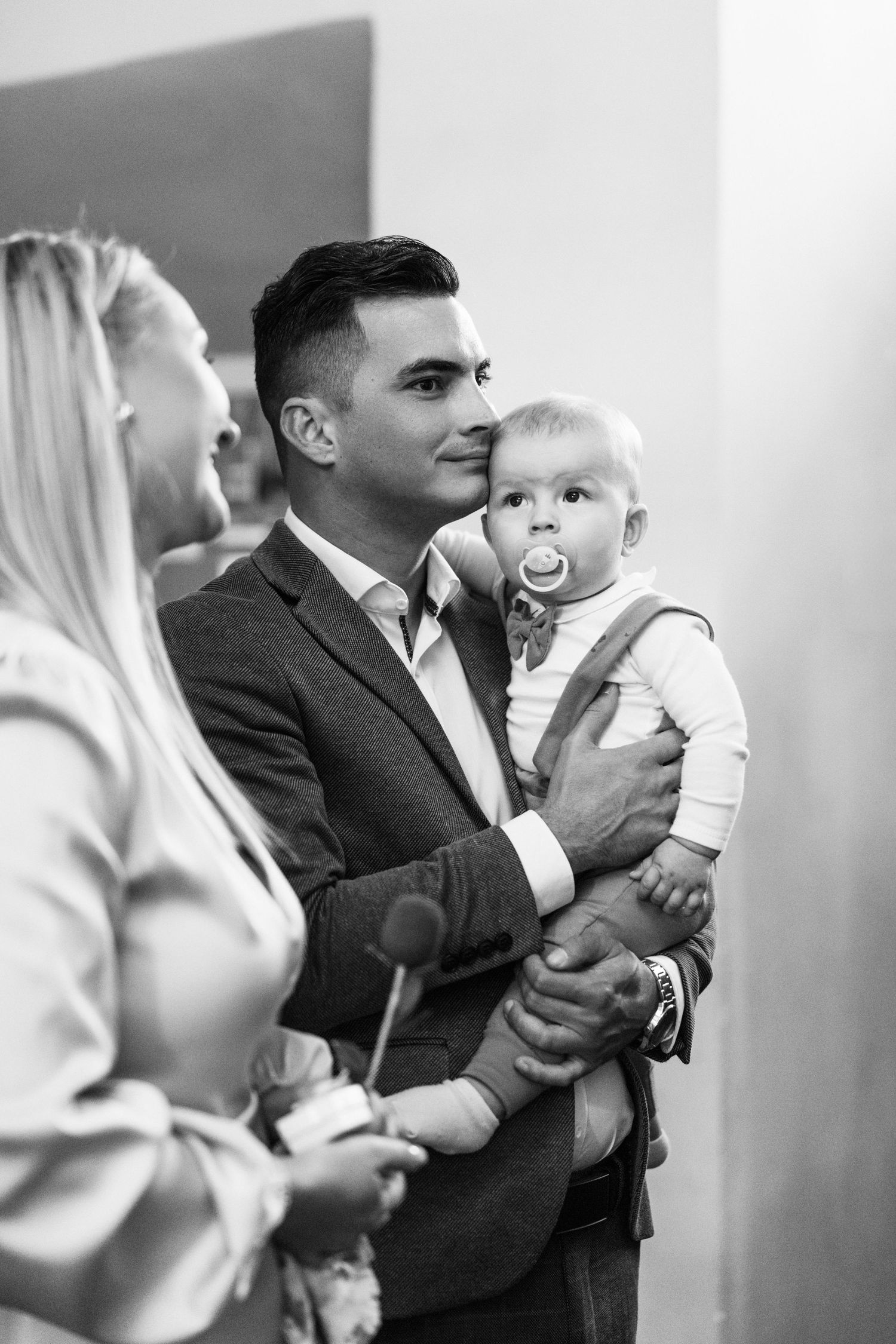 Black and white photos showing tender moments between a baby in white clothing and adults in formal attire.