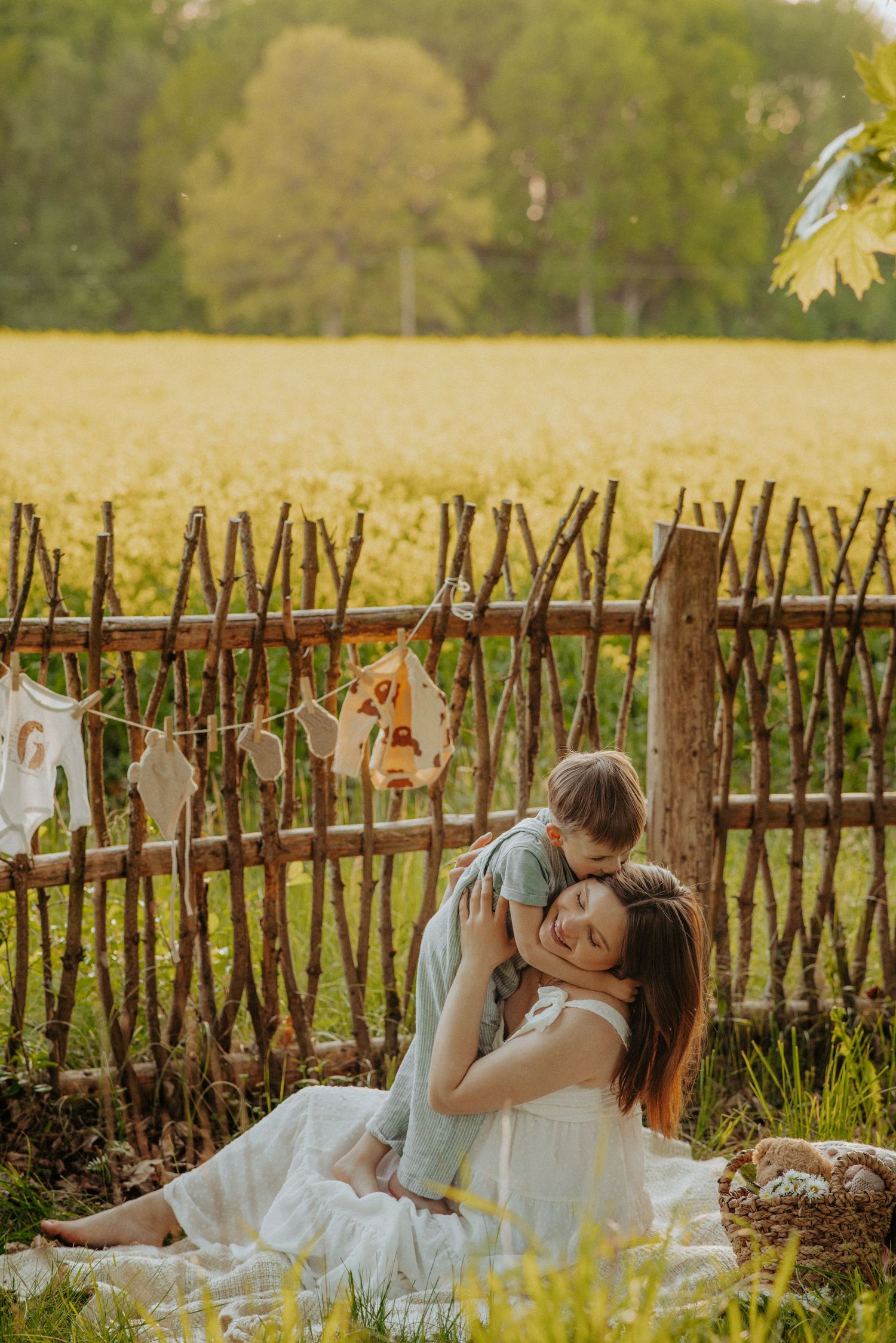 Intimate maternity moment shared on a blanket by rustic wooden fence at golden hour.