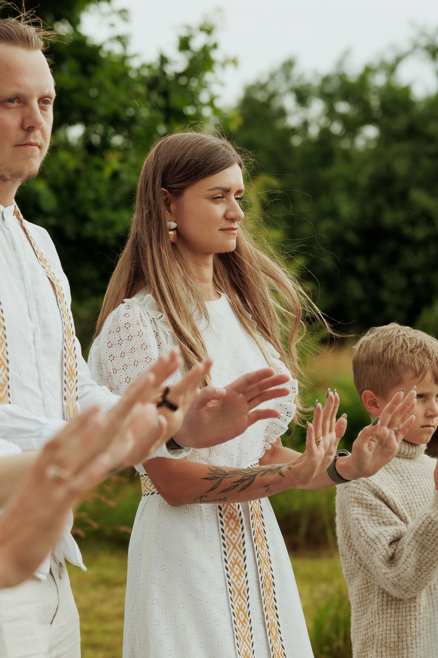 Woman and boy in traditional embroidered white attire clapping hands during an outdoor ceremony.