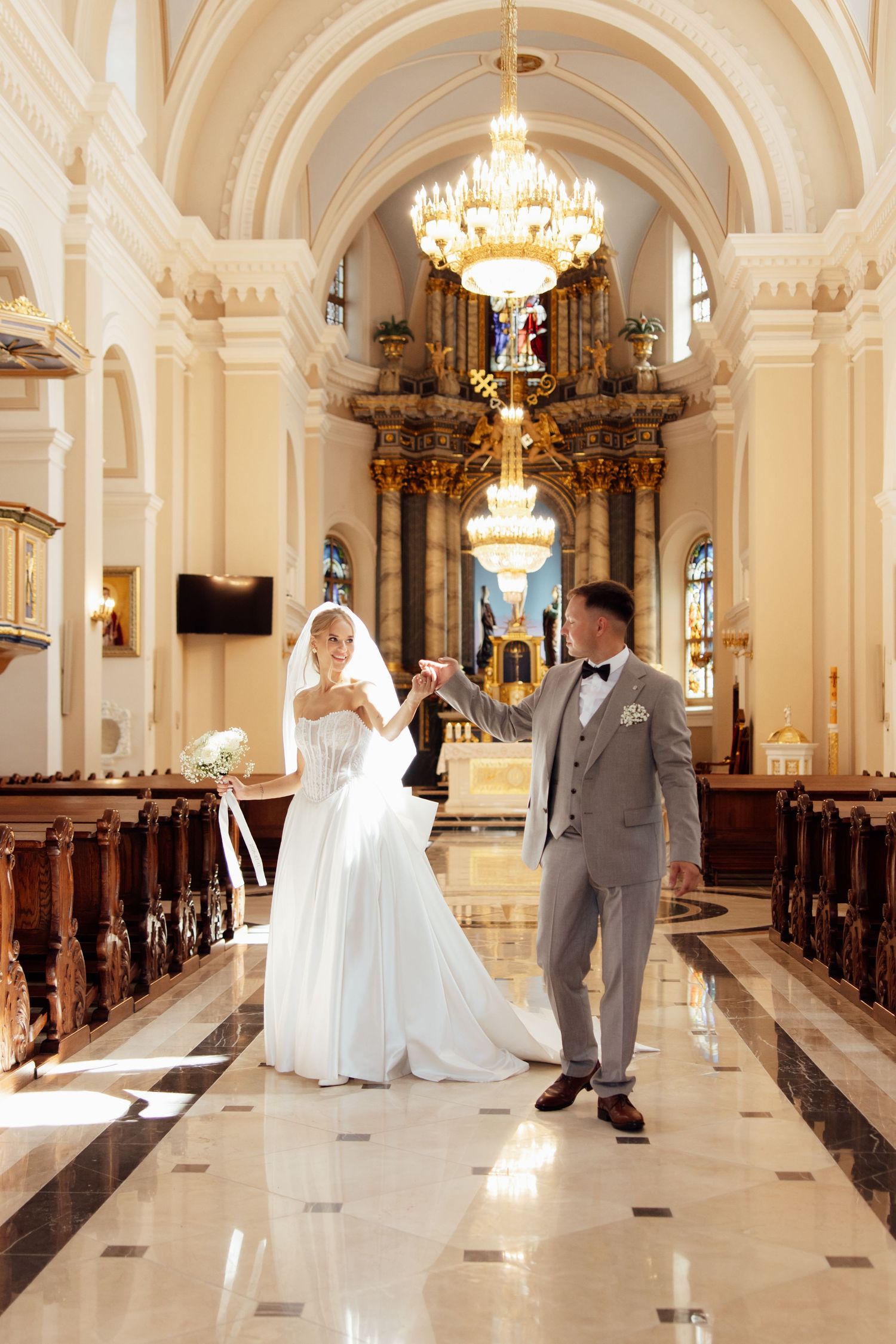 Bride and groom hold hands walking down the aisle of an elegant church with ornate gold altar.