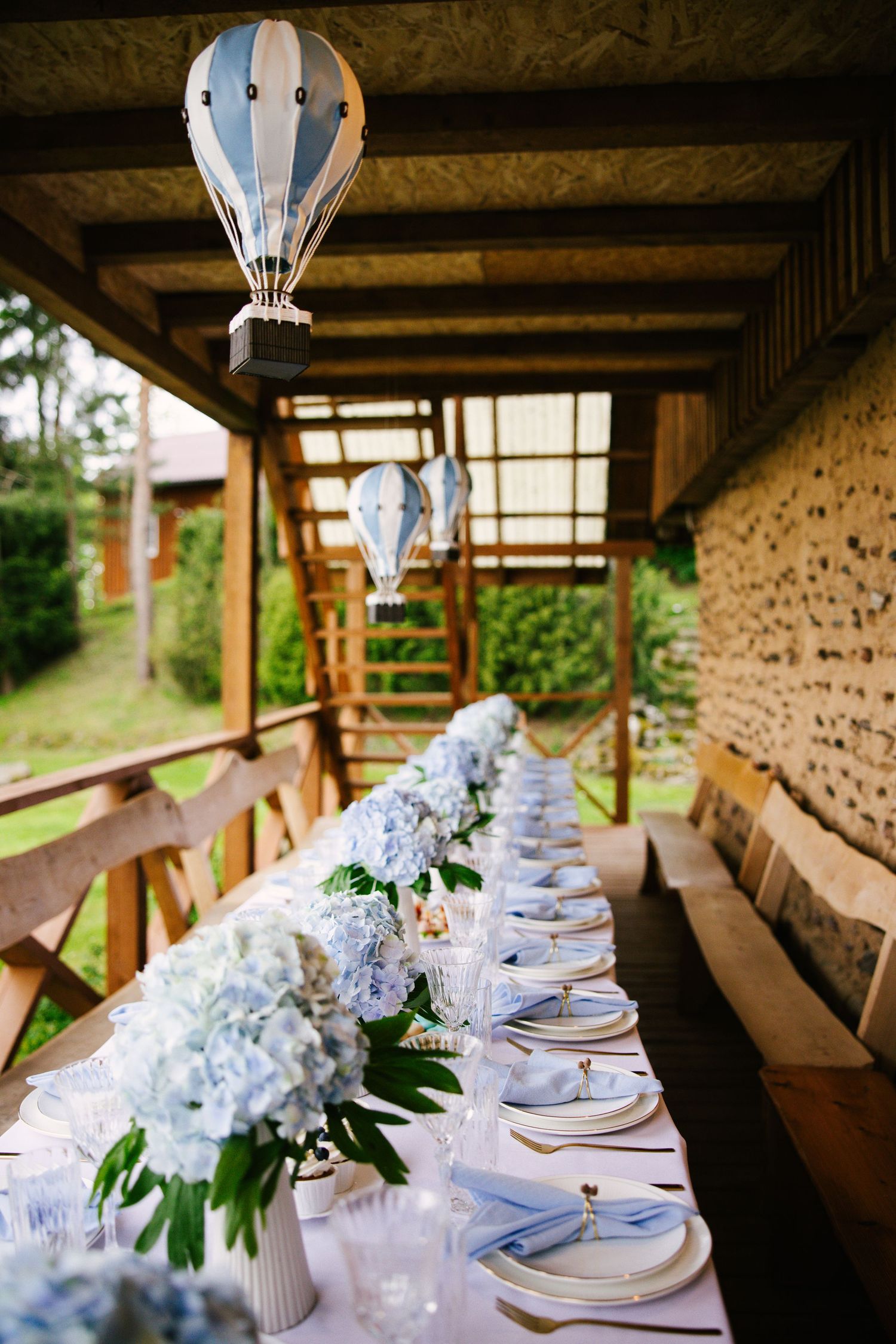 Elegant table setting with blue hydrangeas and hanging hot air balloon decorations in rustic venue.