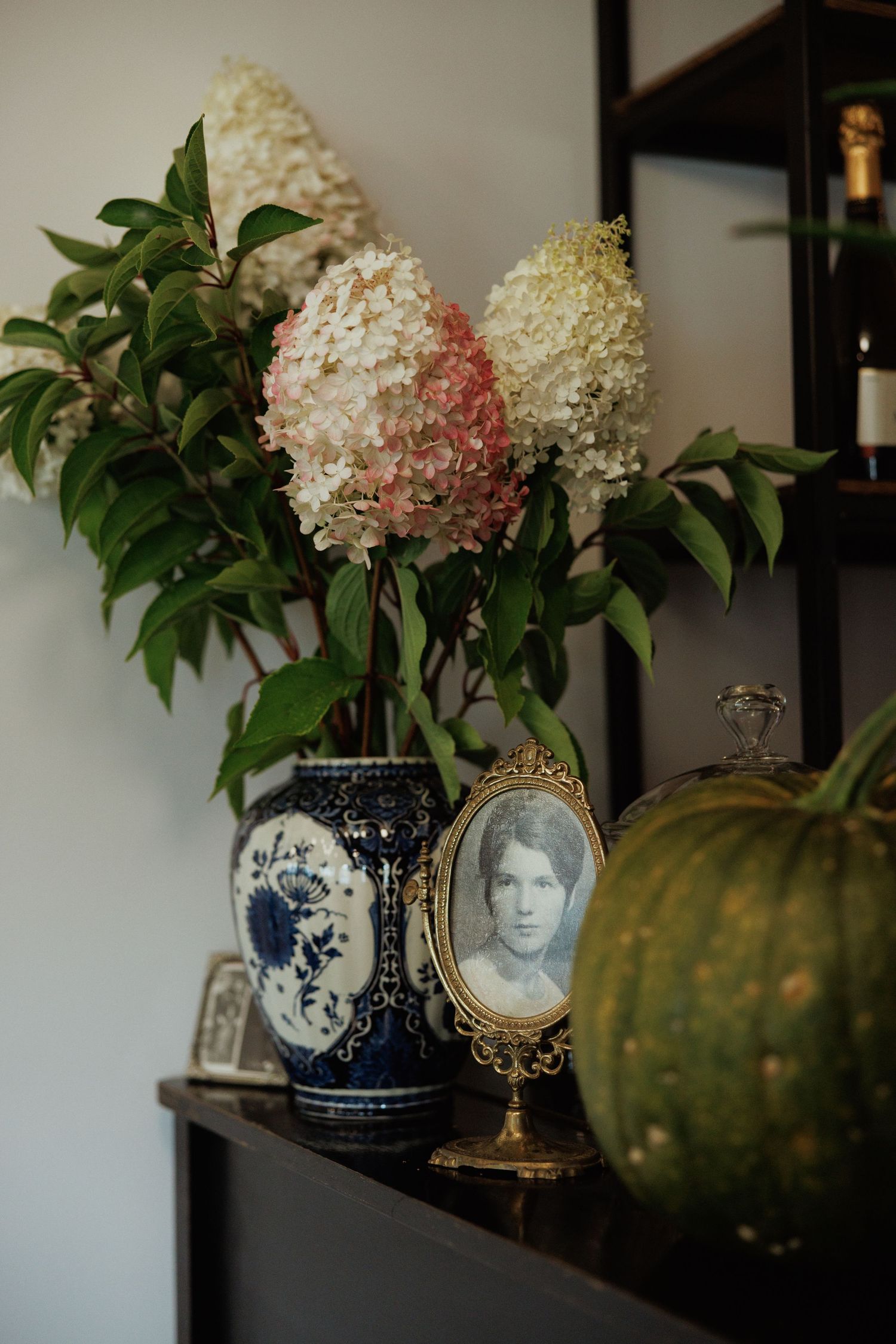 Hydrangea arrangement in blue and white vase with vintage decor and green pumpkin.