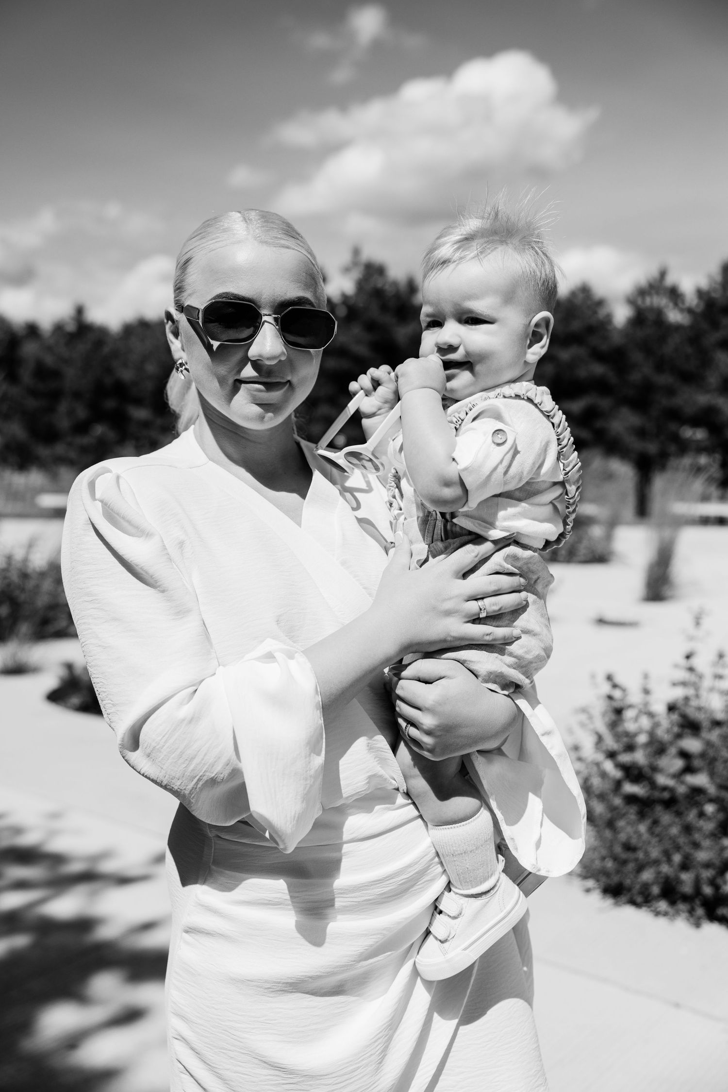 Black and white photo sequence of a parent holding and playing with a baby outdoors on a sunny day.