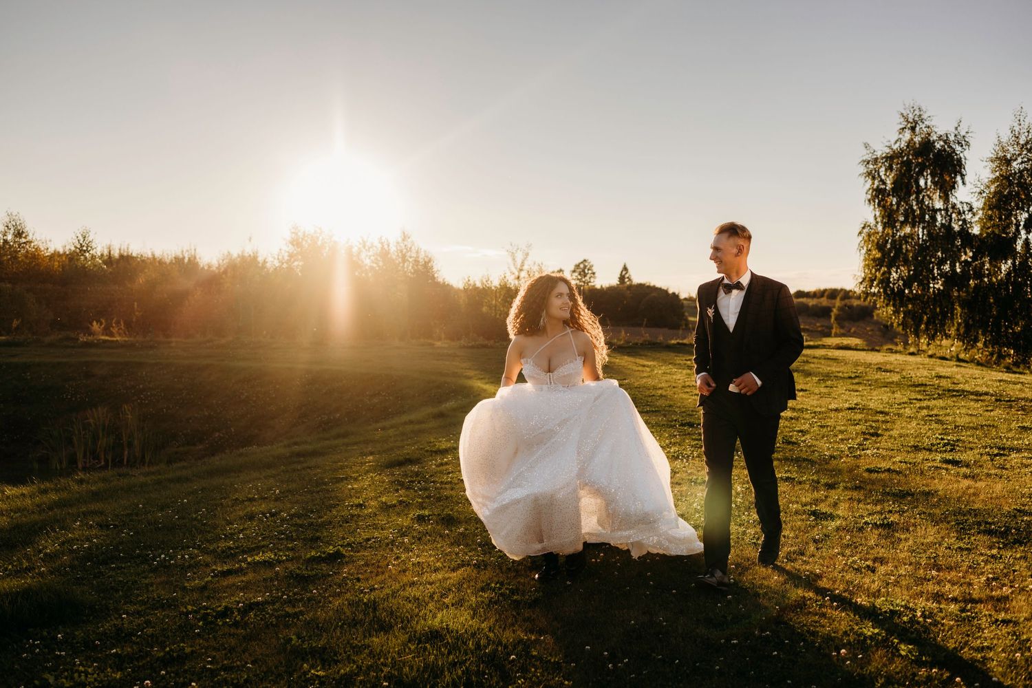 Silhouetted wedding couple walking in golden sunset light across an open field.