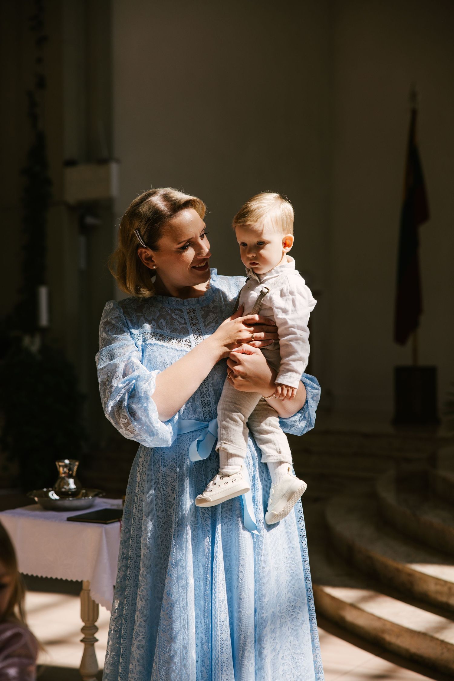 A woman in a light blue dress holds and interacts with a baby in a series of candid indoor photographs.