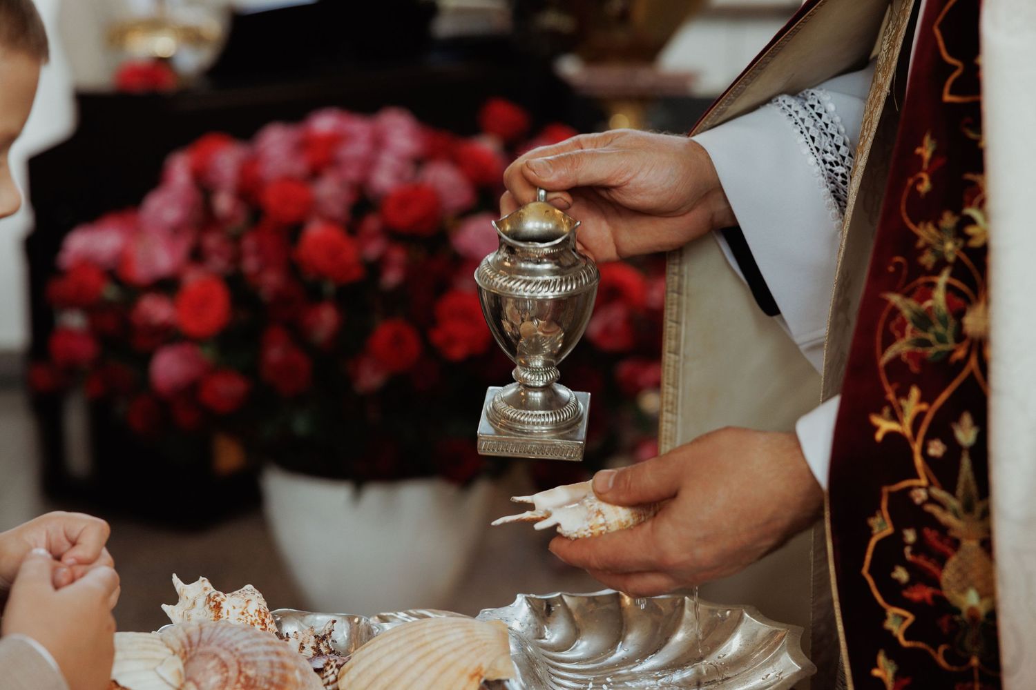 Close-up view of hands serving elegant desserts at a formal event with red floral arrangements in background.