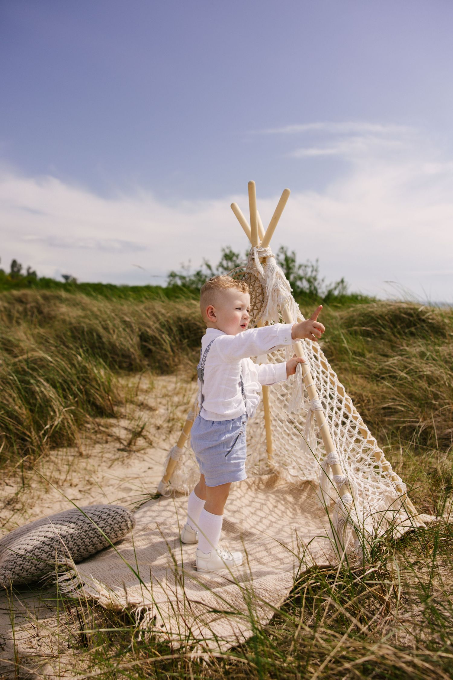 Beachy scene with teepee setup and child playing in sand dunes.