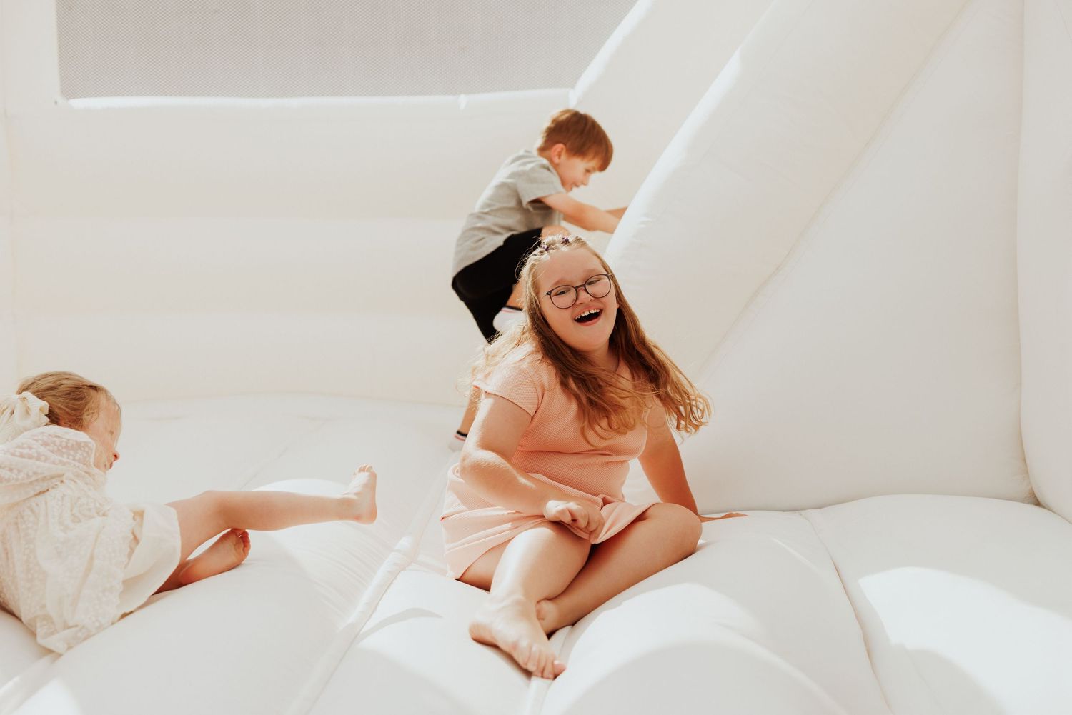 People playing and climbing on white inflatable bounce surface indoors.